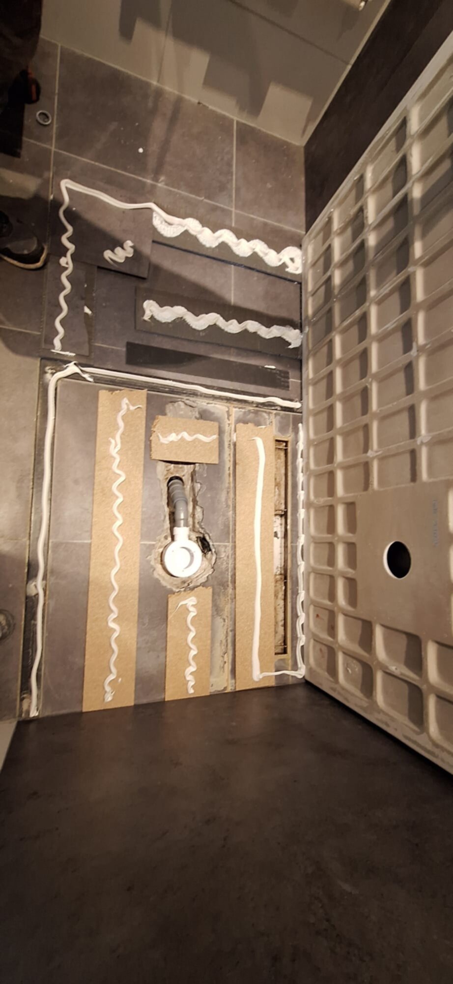 Grijs betegelde badkamer in renovatie fase met opengelegd leidingwerk
