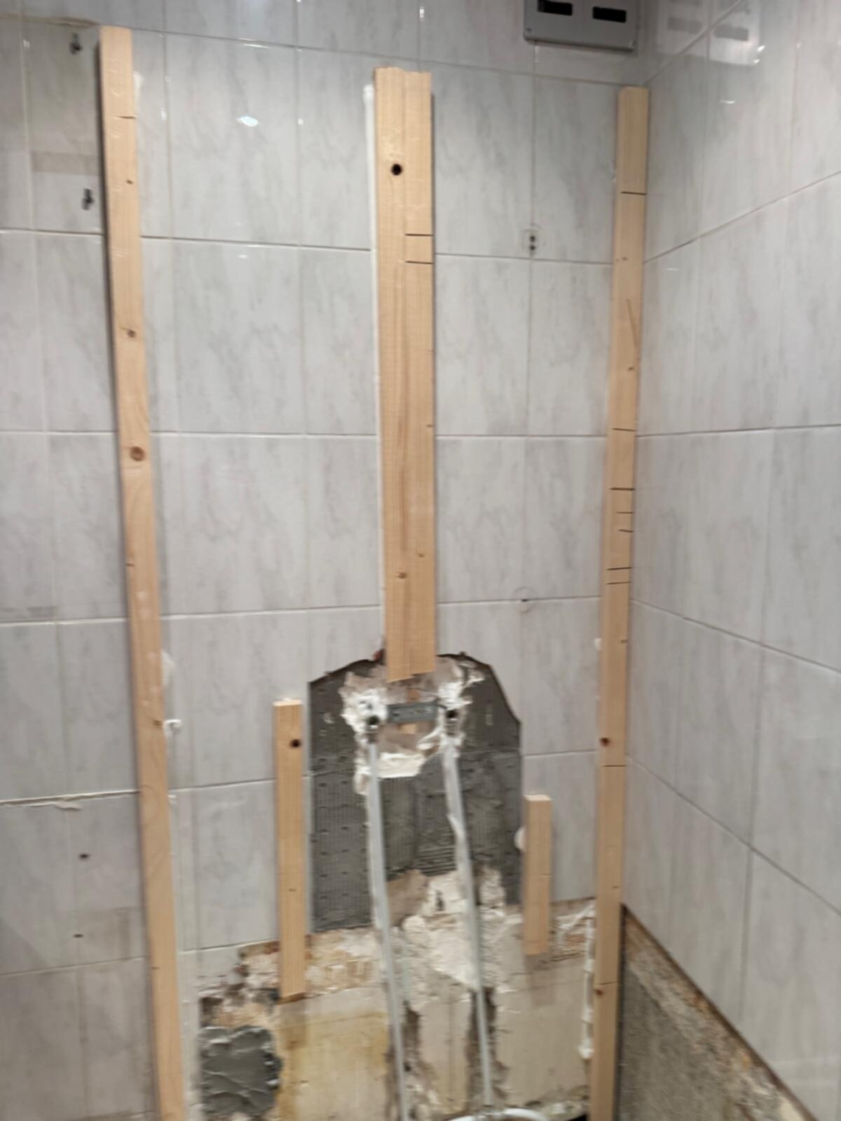 Badkamer renovatie, houten latten tegen betegelde muur, kapotte stuk muur