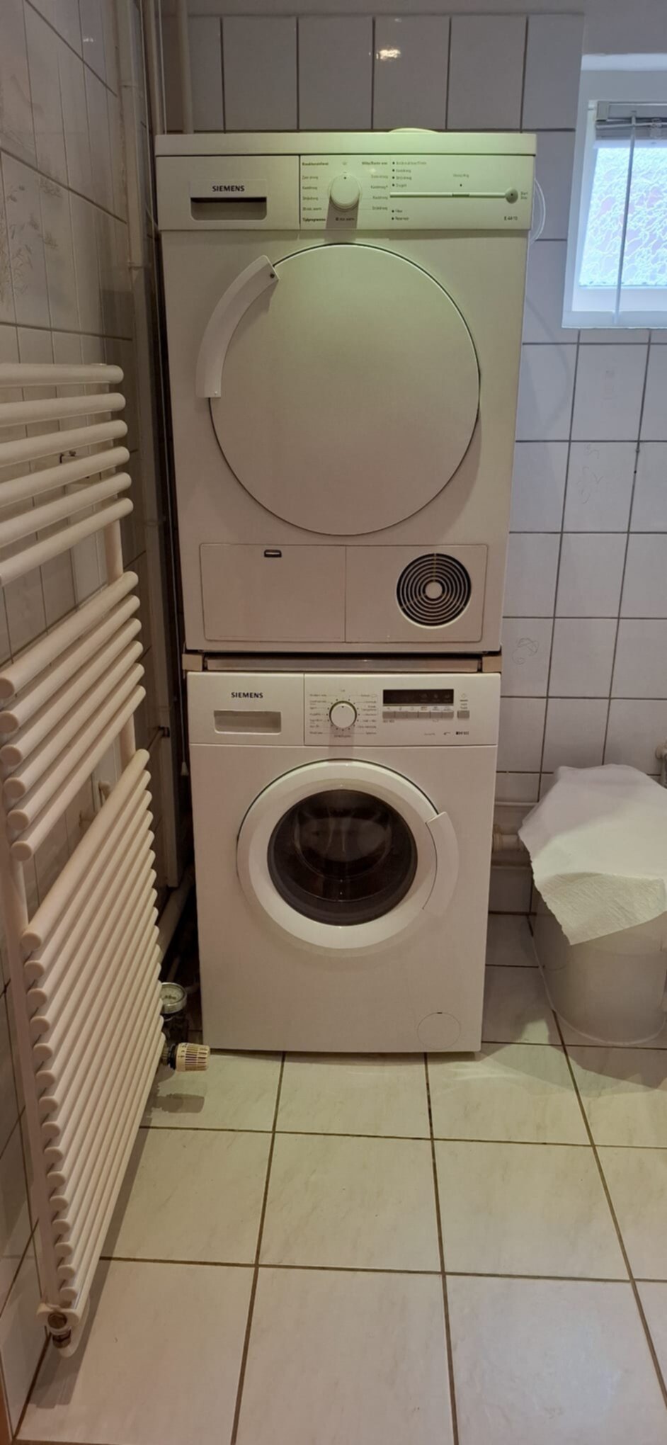 Wit betegelde badkamer met wasmachine en droger op elkaar gestapeld