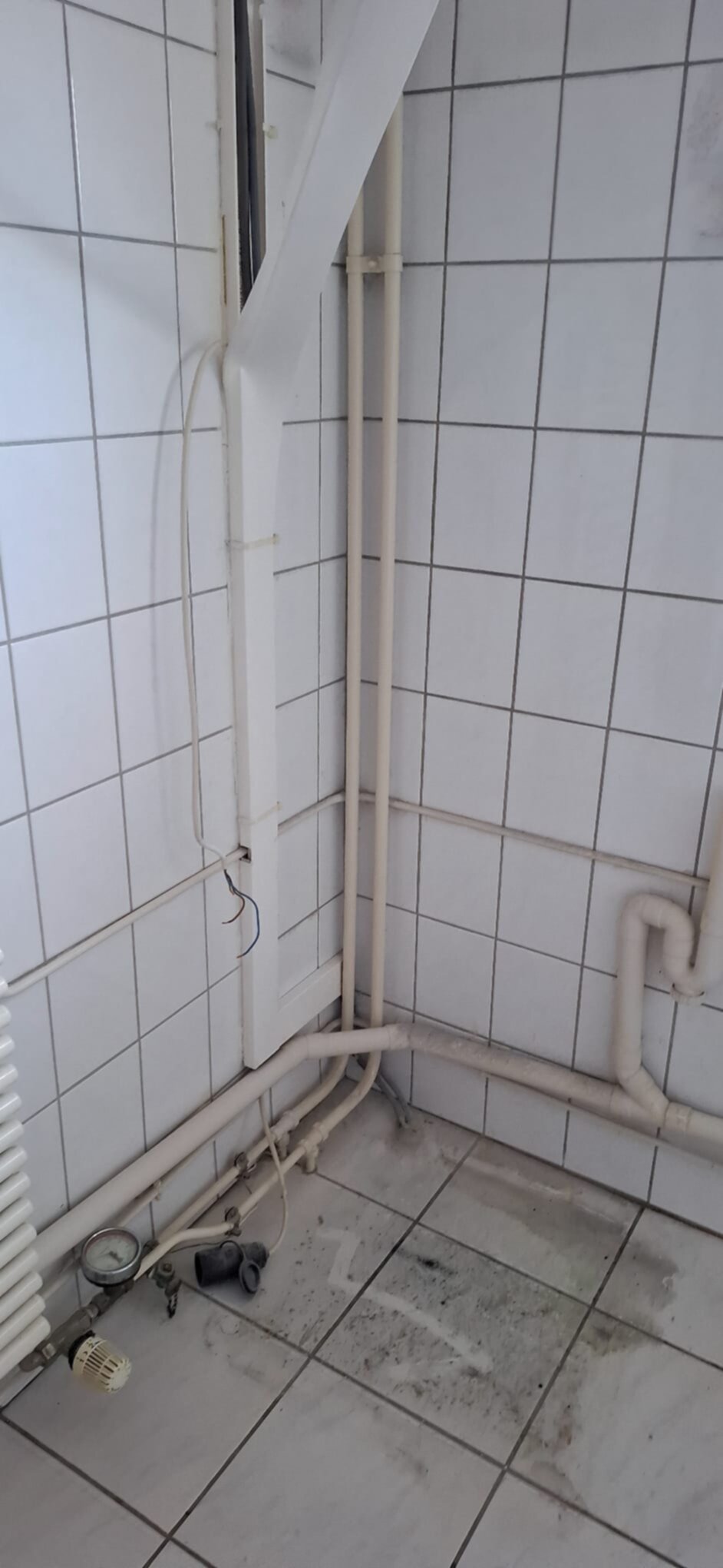 Slechte staat badkamer met witte tegelwanden en -vloer en zichtbare leidingen