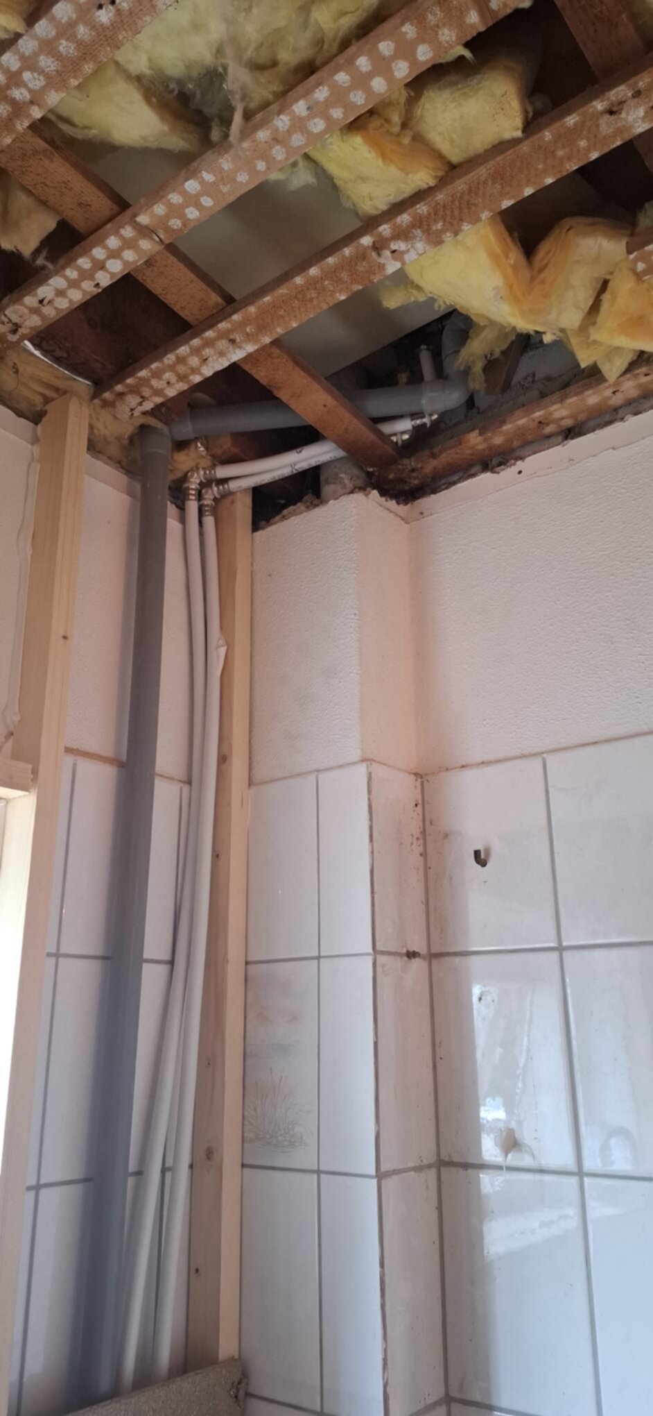 Open badkamer met blootgelegde leidingen en houten dakconstructie tijdens renovatie