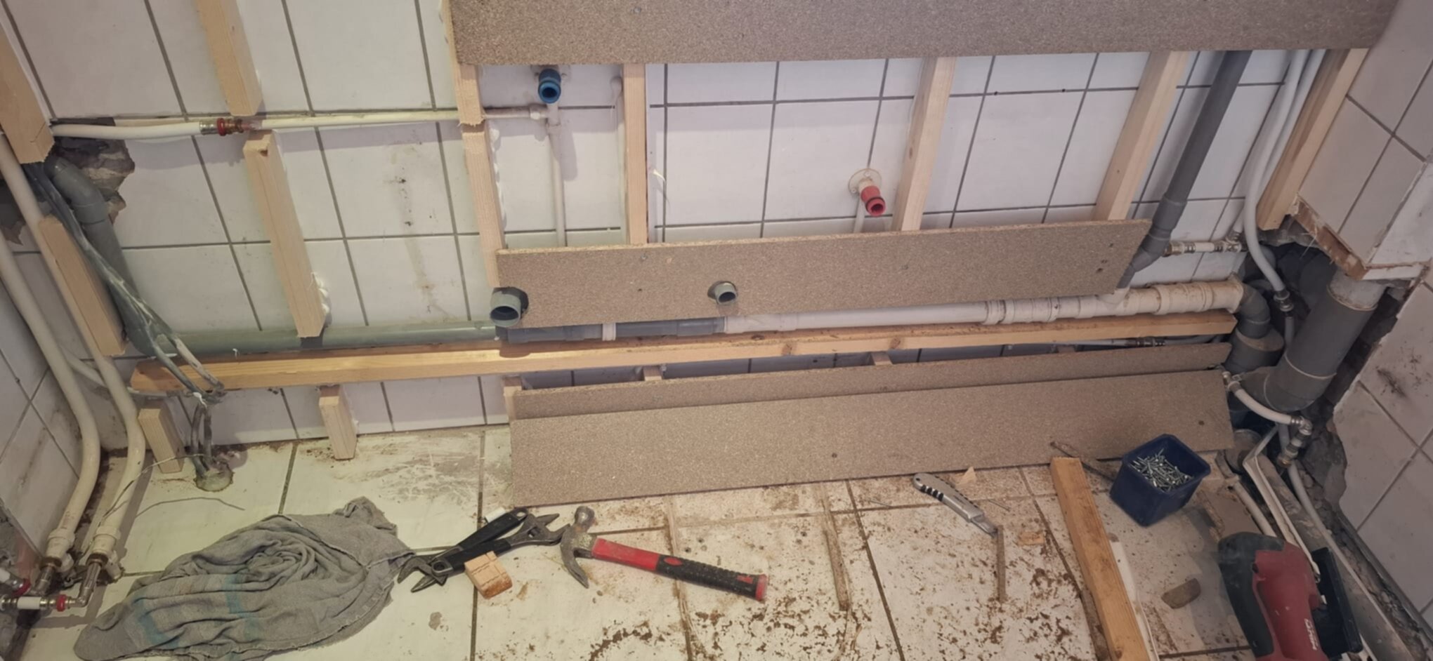 Badkamer renovatie in uitvoering, zicht op de betegelde muur en open leidingen