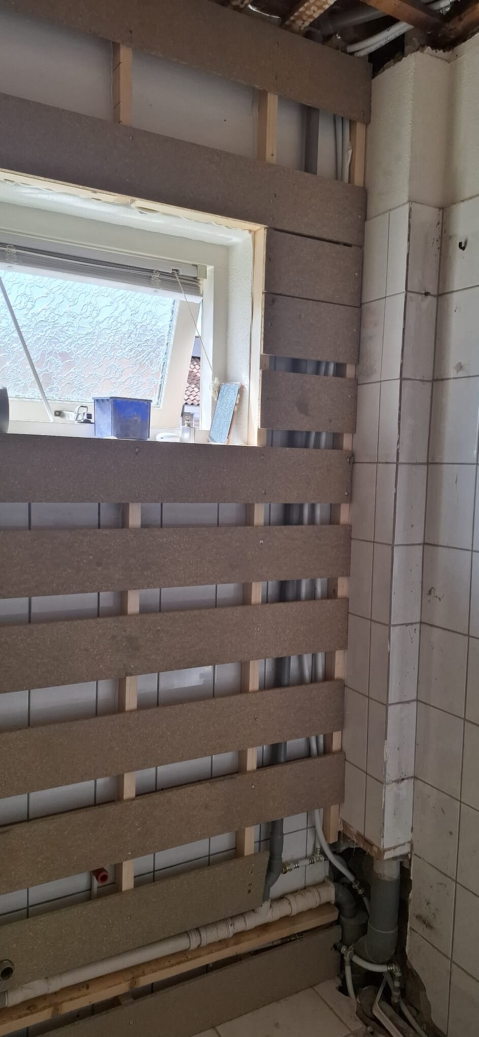 Badkamer in renovatie, houten panelen voor betegeling, blootgelegde leidingen en oude tegels