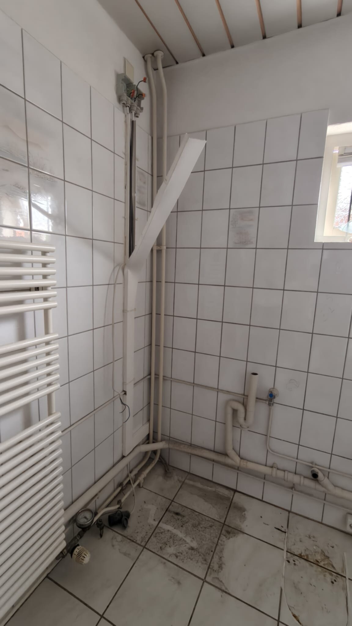 Slechte staat badkamer met witte tegels en zichtbare leidingen