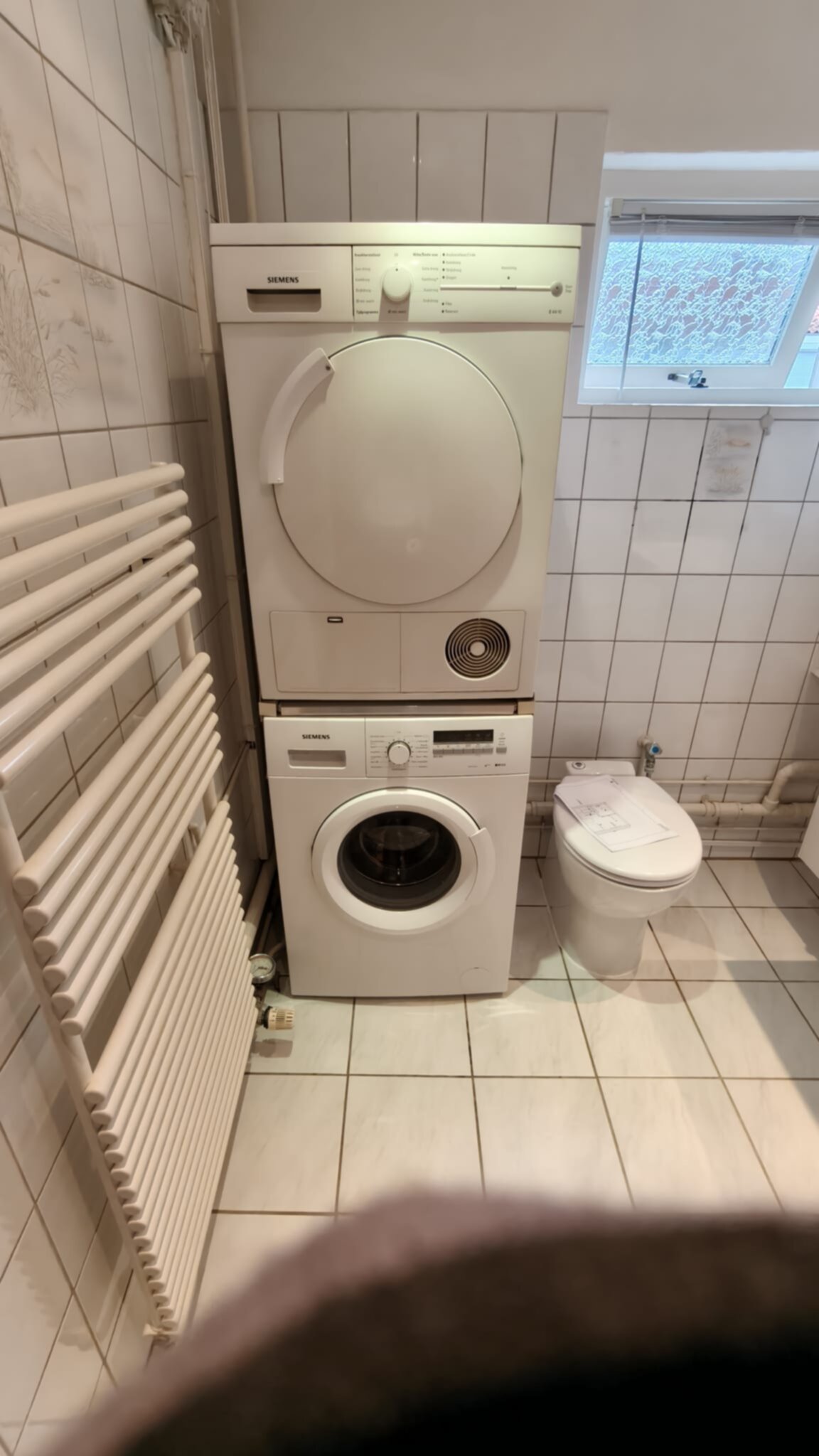 Wit betegelde badkamer met wasmachine en droger en toilet