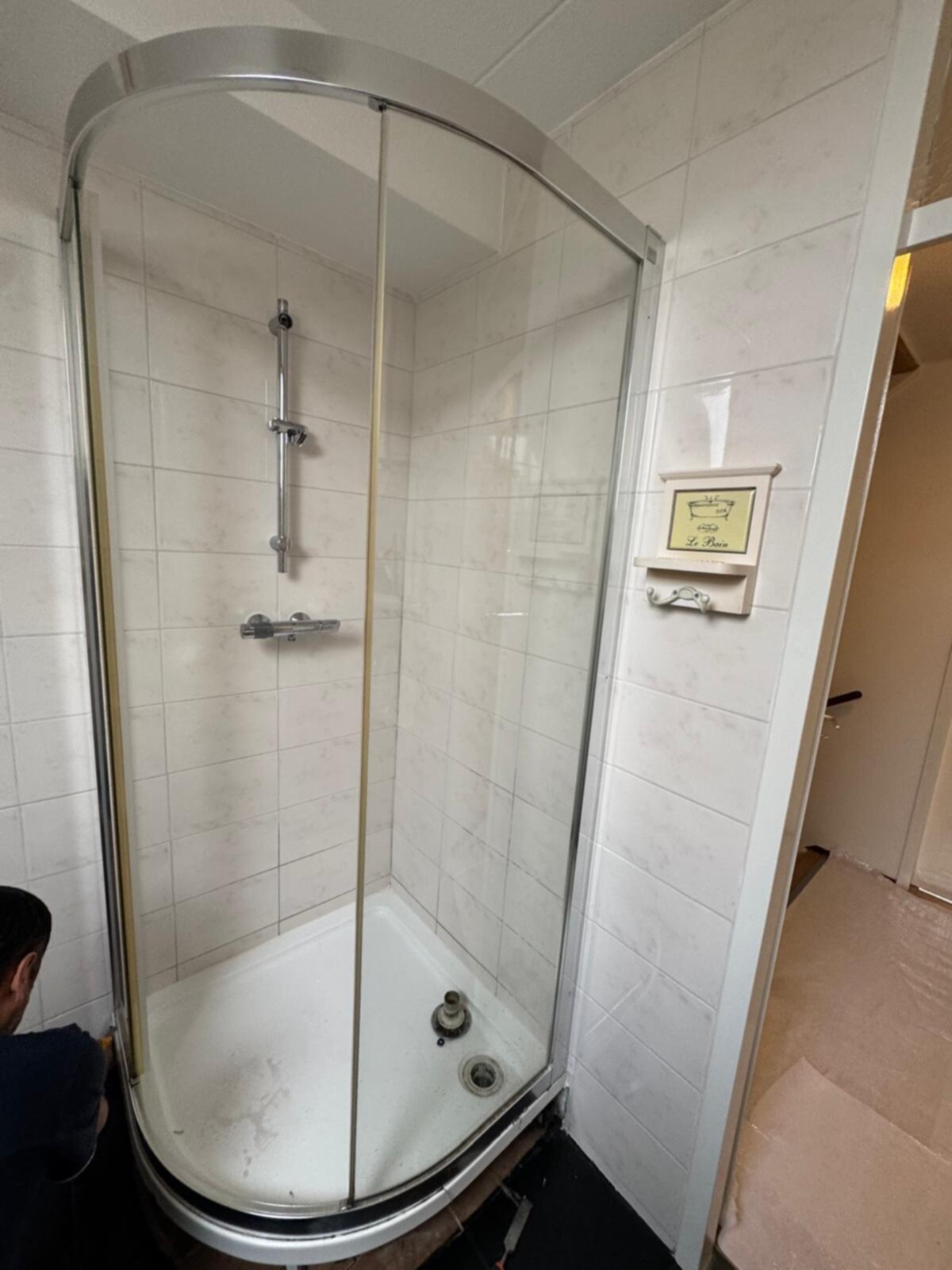 Douchecabine met witte tegelwanden en glazen deur in renovatie fase