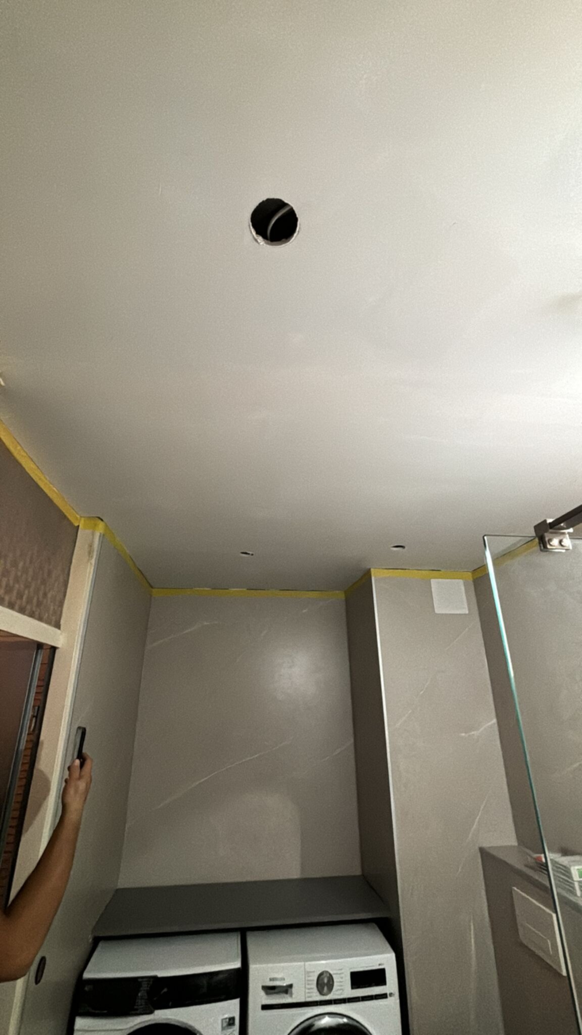 Schilderwerk in badkamer, plafond en muren in lichtgrijze kleur, wasmachine en droger zichtbaar