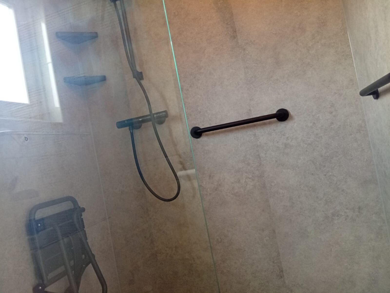 Douche met beige betegeling en zwarte accessoires, inclusief douchekruk en handgreep