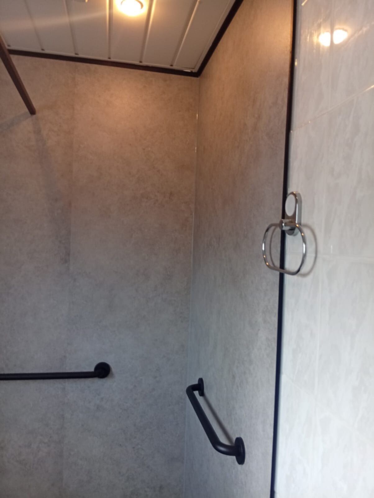Douche met beige tegels en zwarte grepen voor toegankelijkheid