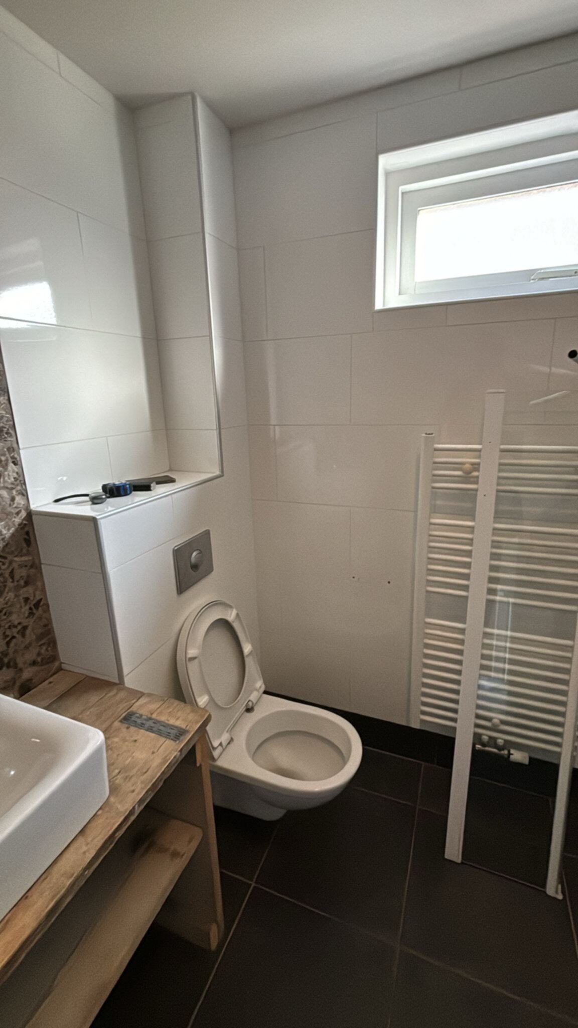 Wit betegelde badkamer met toilet, wasbak en verwarming