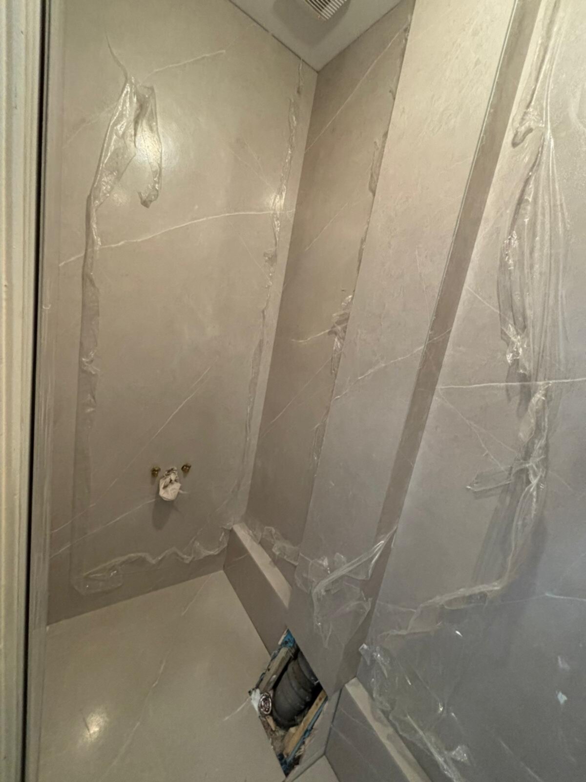 Badkamer tijdens renovatie met grijze marmeren tegels en plastic bescherming