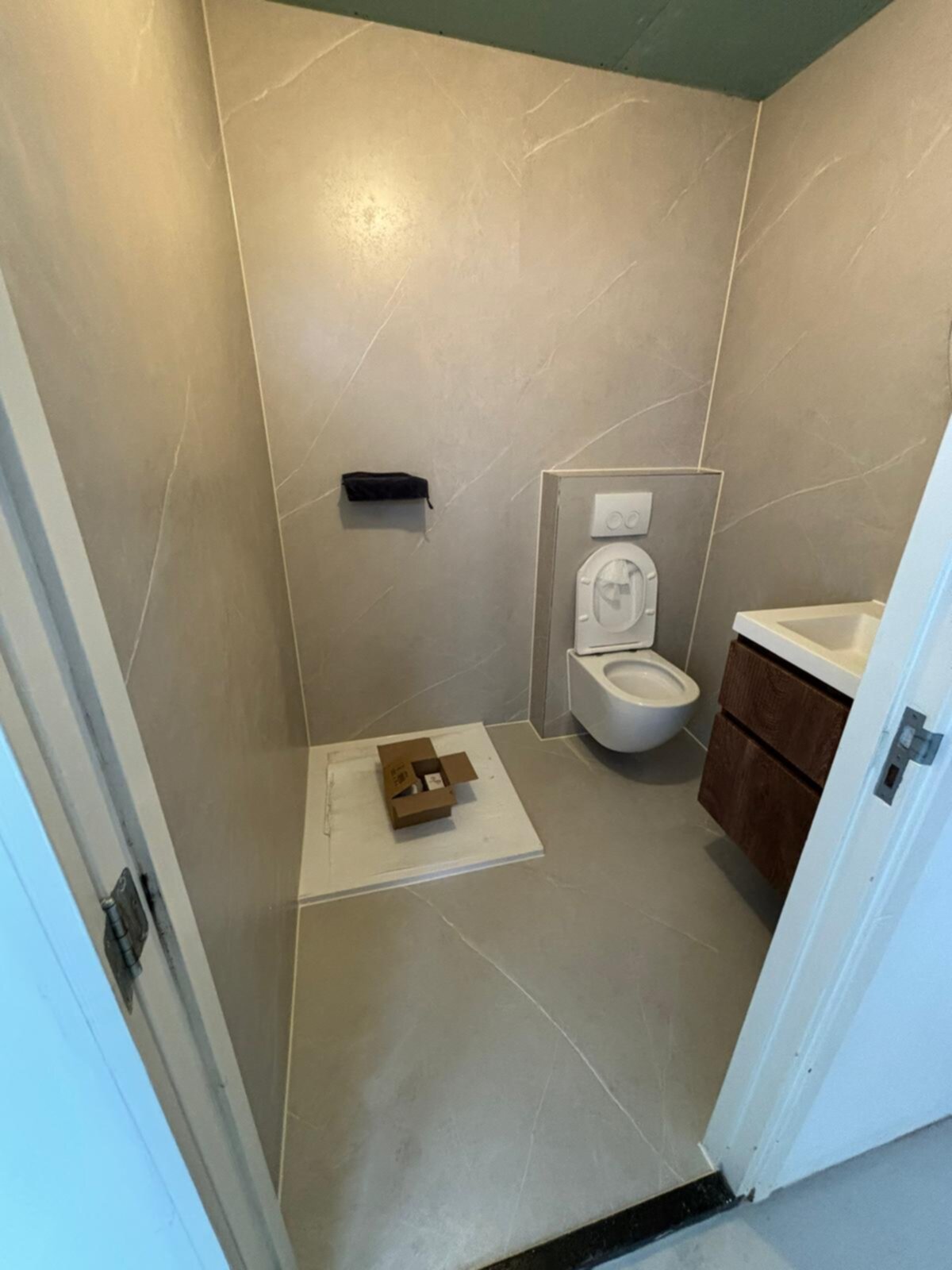 Grijze betegelde badkamer met toilet, wastafel en betegelde vloer tijdens renovatie