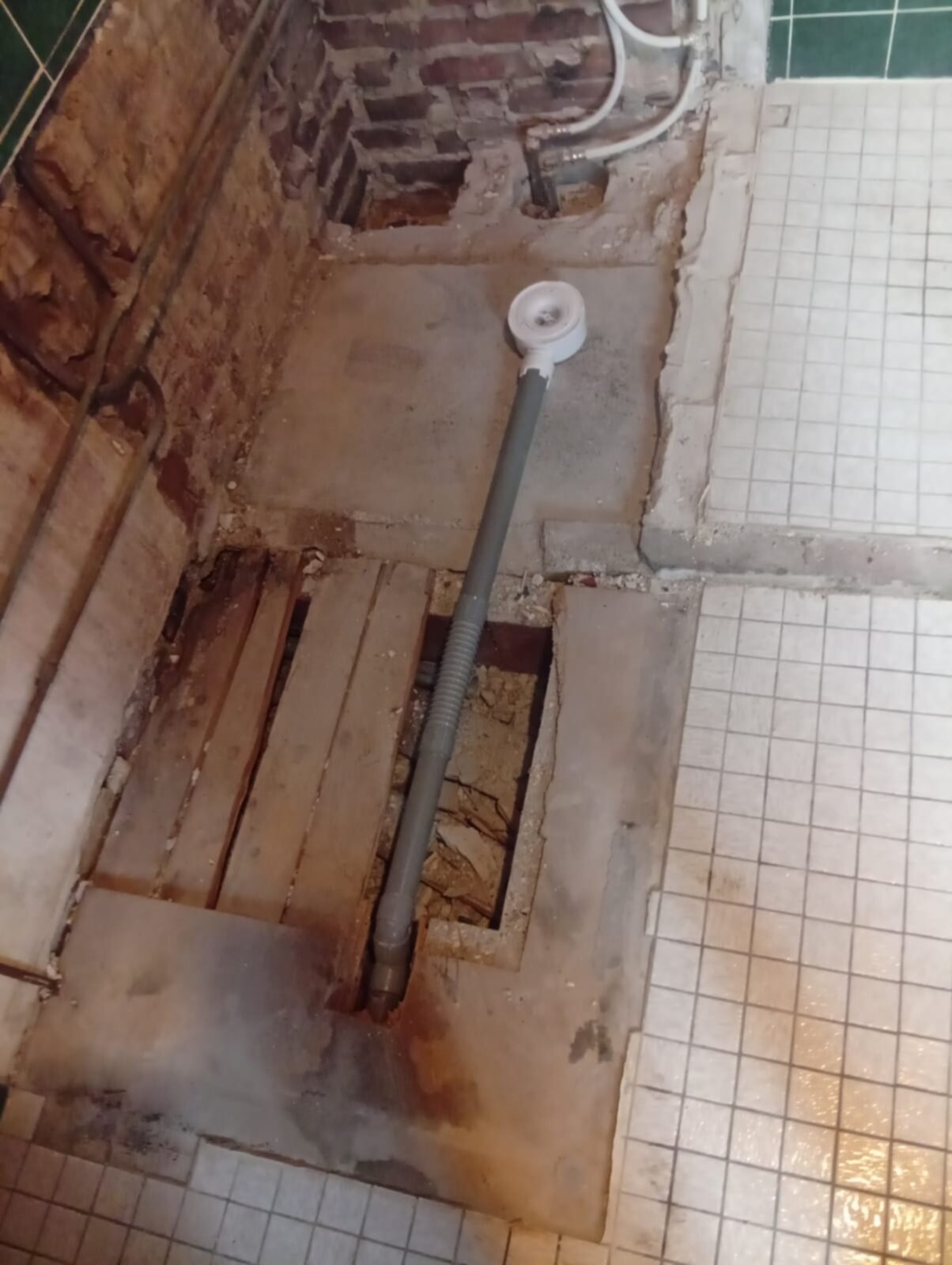 Sleuf in badkamer vloer met blootgelegde rioleringsbuis en houten vloerdelen