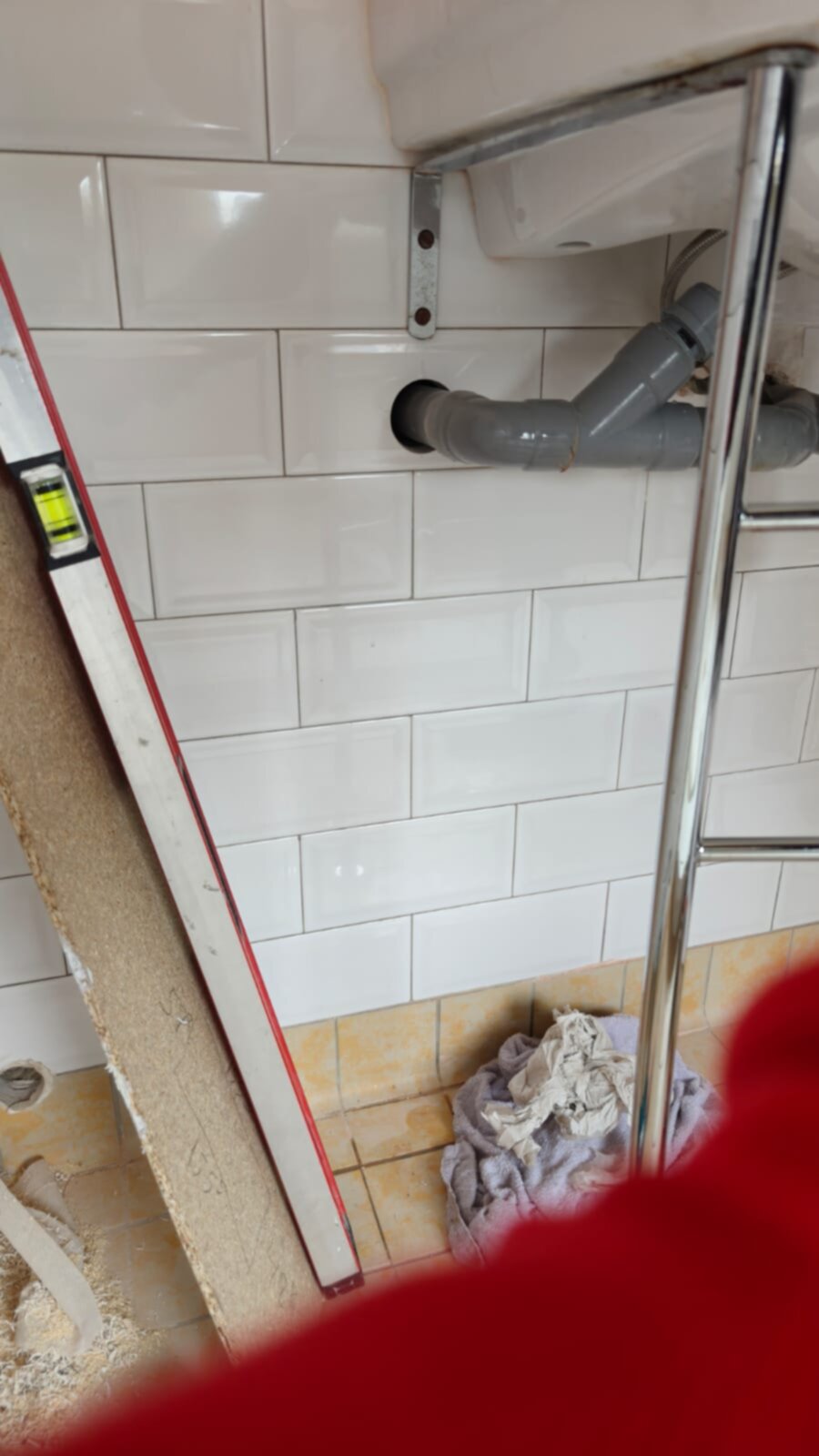 Wit betegelde badkamerwand met grijs PVC rioolbuis en werkmaterialen