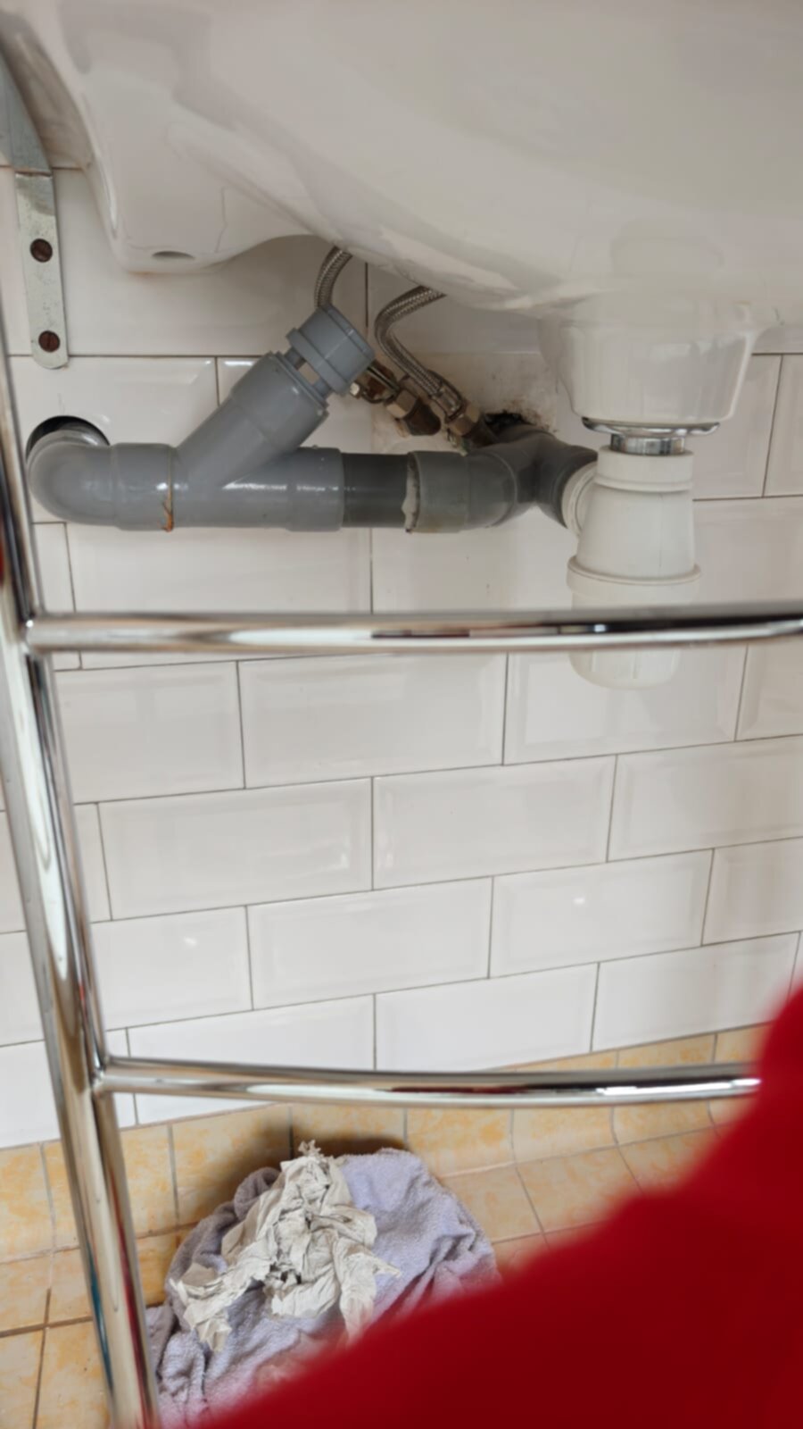 Wit betegelde badkamer met grijs PVC rioolbuis en metalen rek