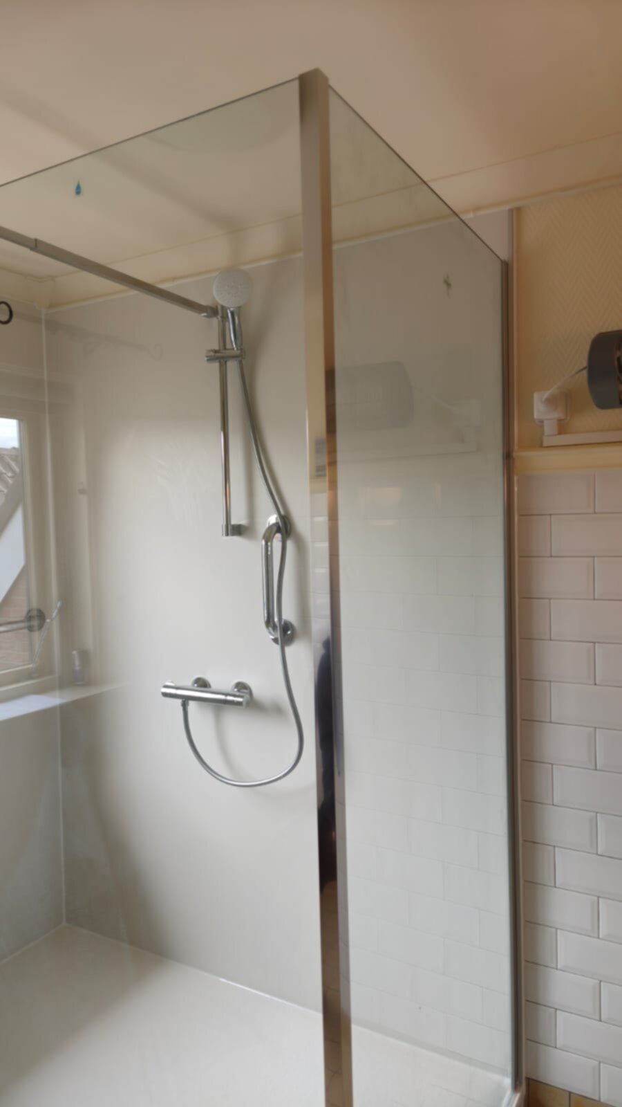 Douchecabine met glazen wand en chroom douchekraan in witte tegelbadkamer