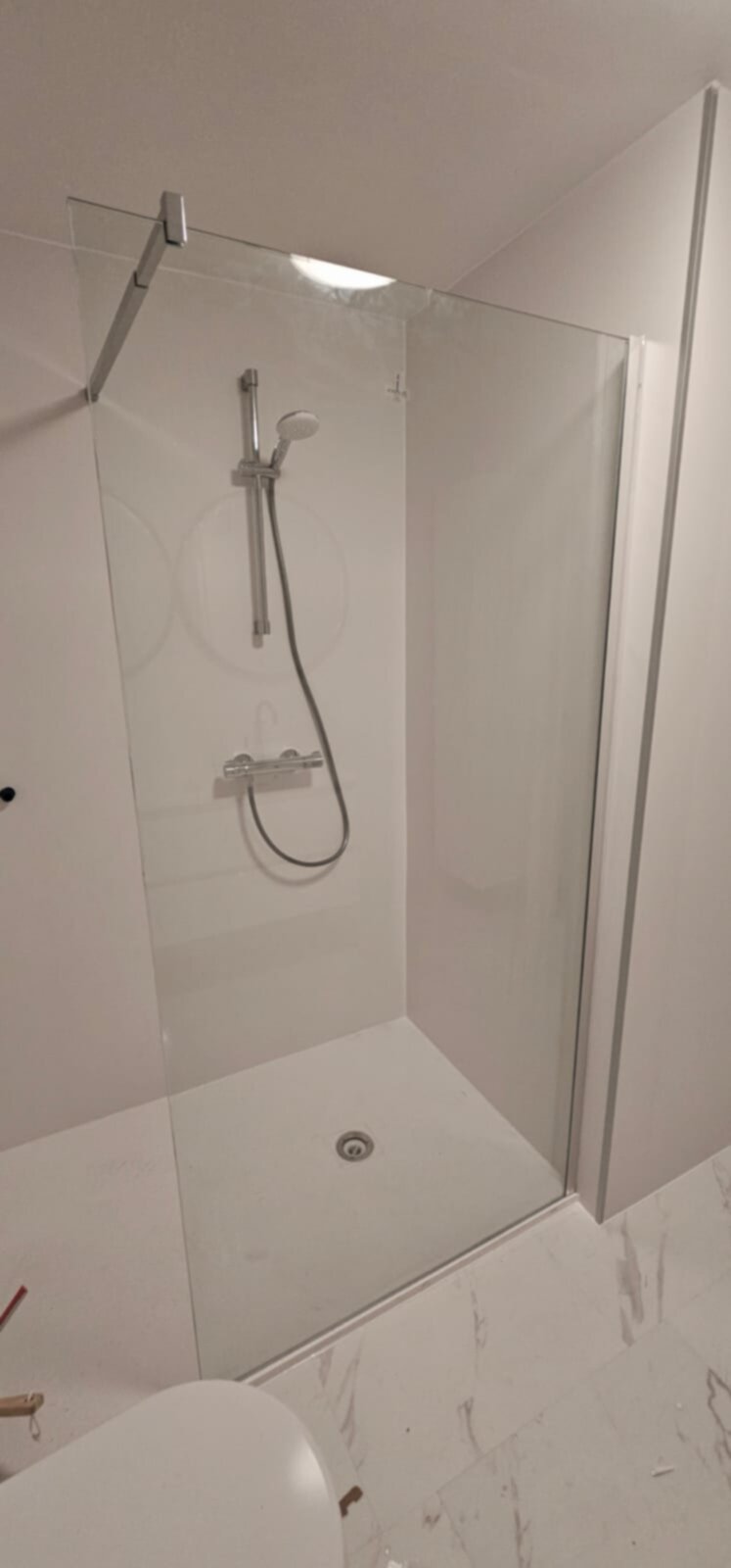 Douchecabine met glazen wand en deur, witte tegelwanden en -vloer met marmerpatroon