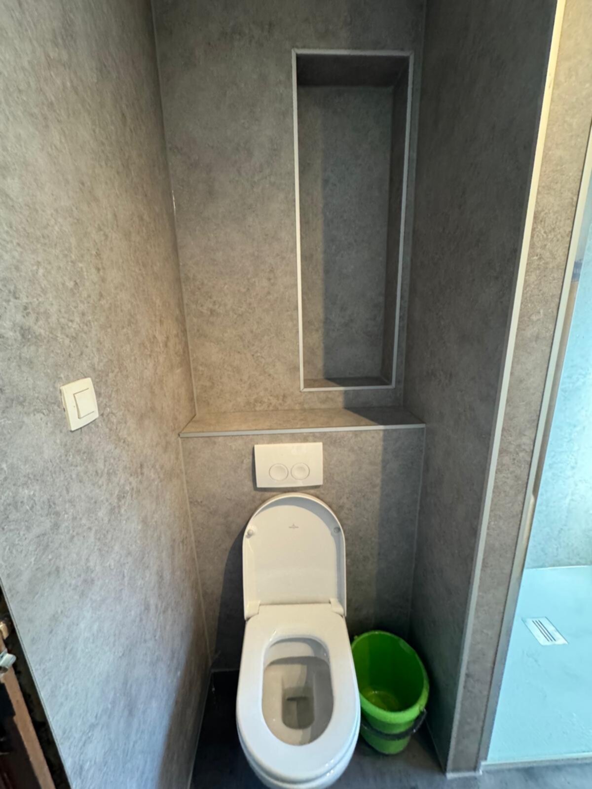 Wit toilet in kleine badkamer met grijze wanden en vloer