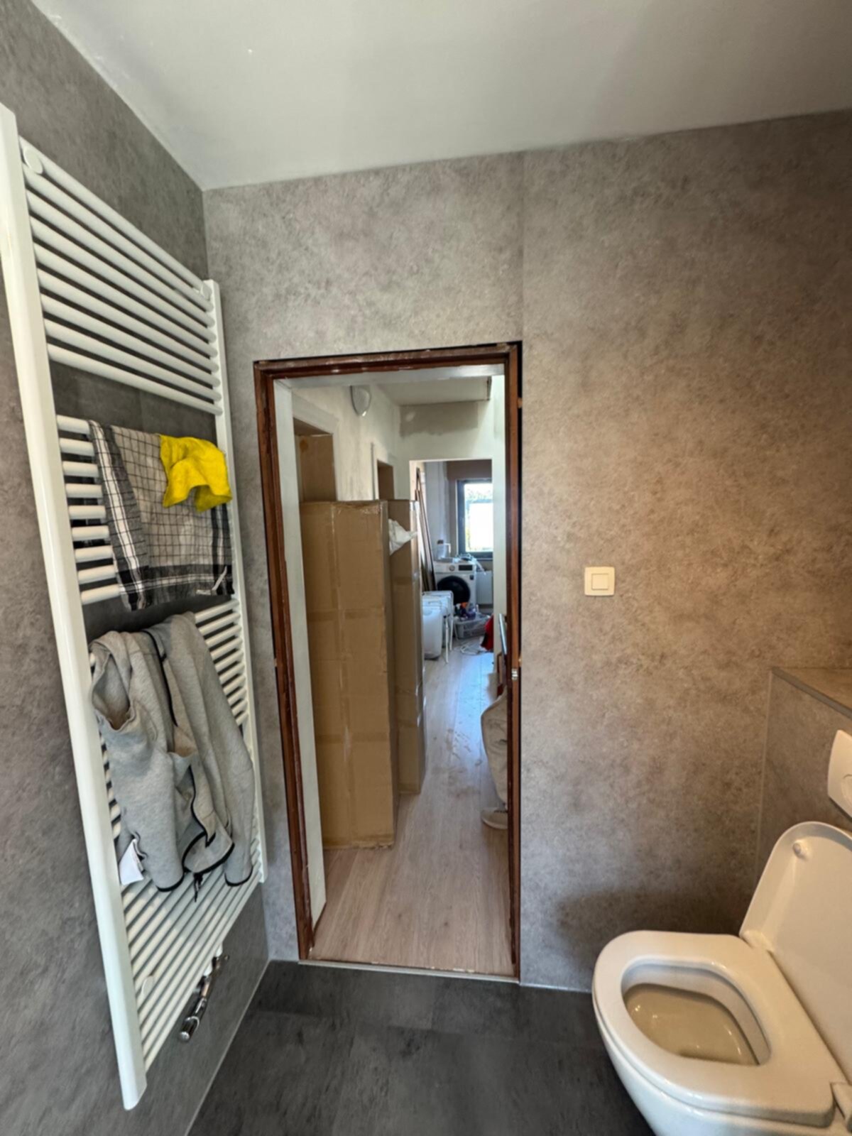 Badkamer met grijze wandtegels, witte toilet en verwarmde handdoekradiator