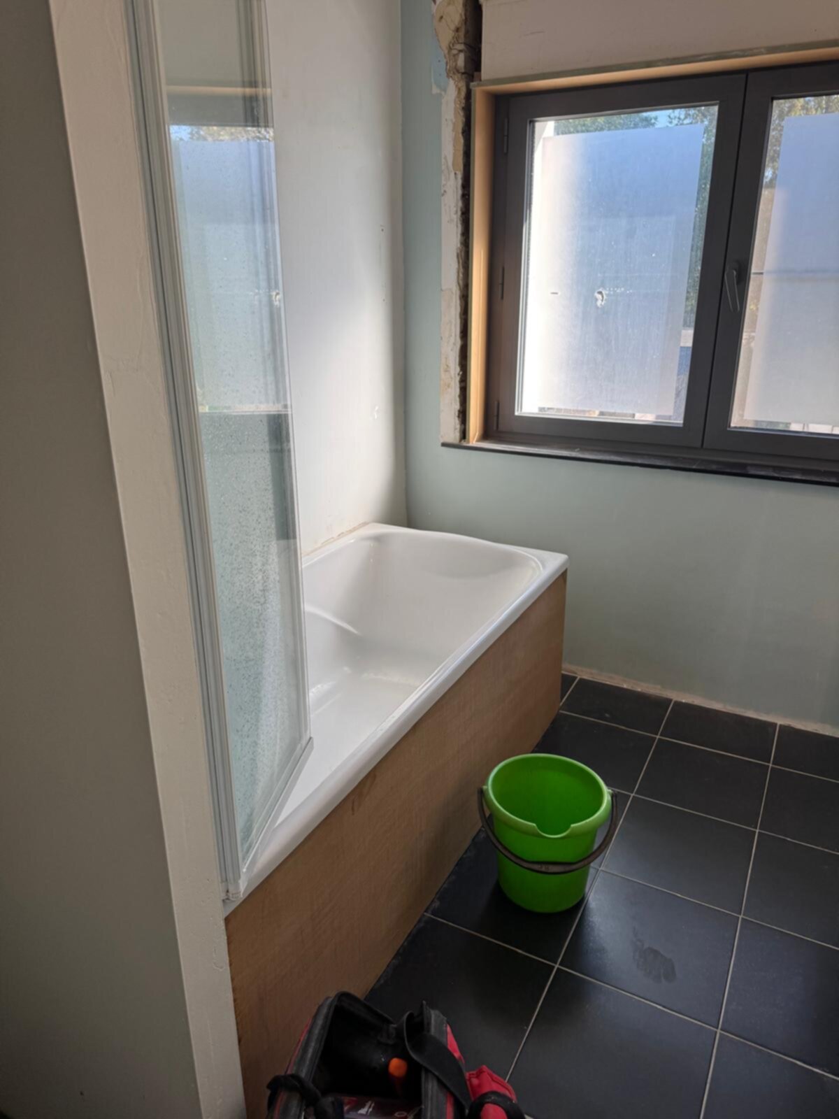 Badkamer in renovatie, witte badkuip en zwarte tegelvloer