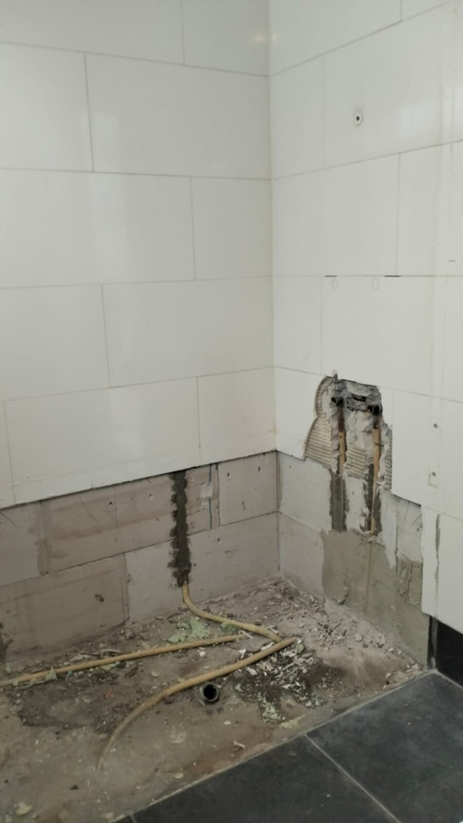 Slechte staat badkamer met kapotte tegelwand en leidingen