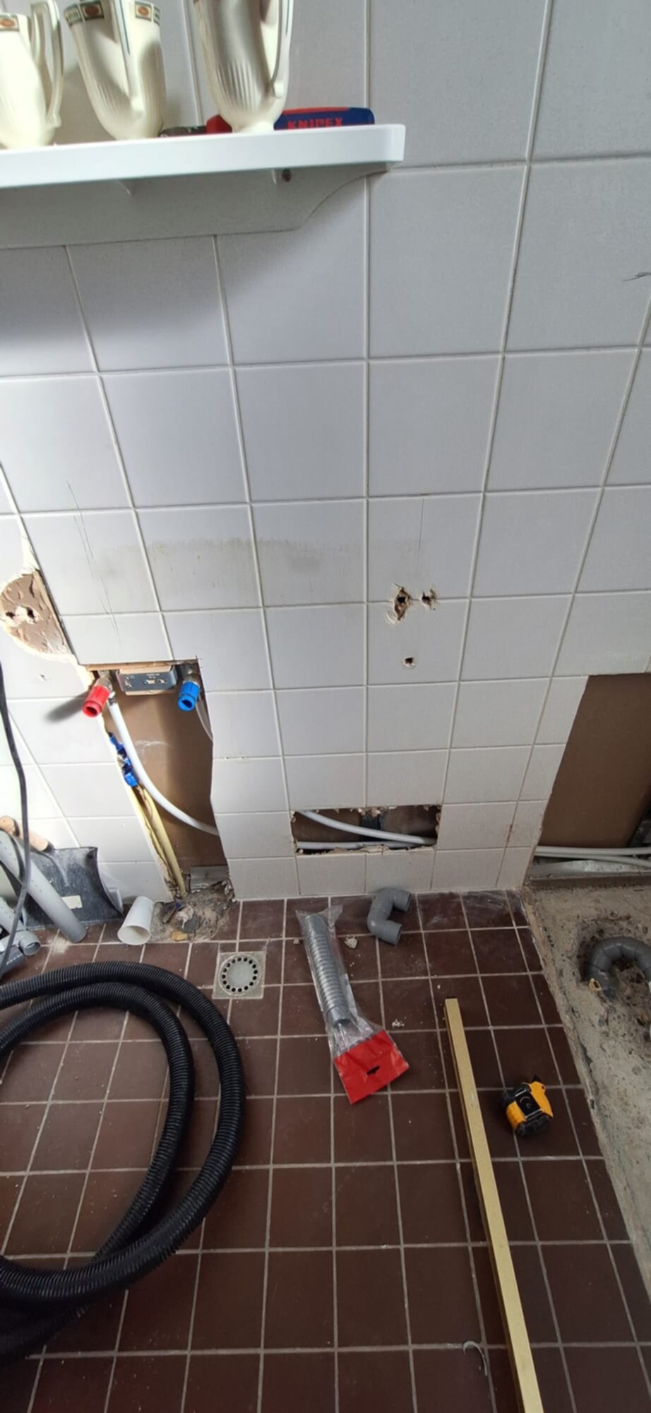 Badkamer renovatie in uitvoering, witte tegelwand deels verwijderd, bruine tegelvloer