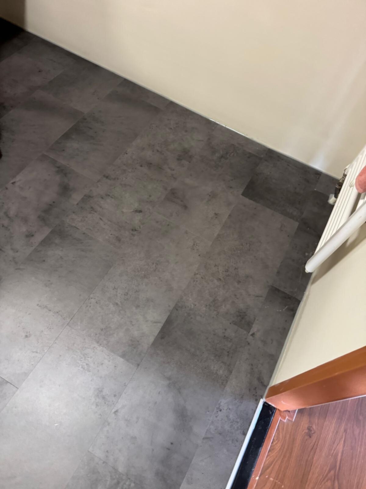 Grijze tegelvloer in een badkamerhoek met witte muren en een bruine deuropening
