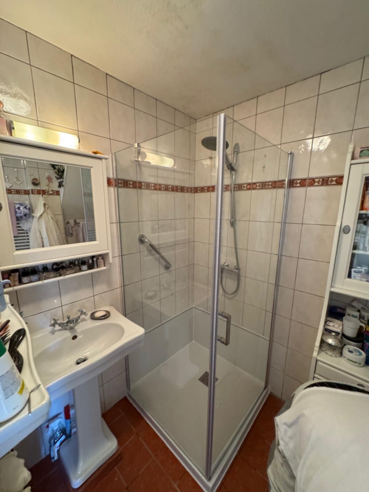 Badkamer met betegelde muren, douche, wastafel en spiegel