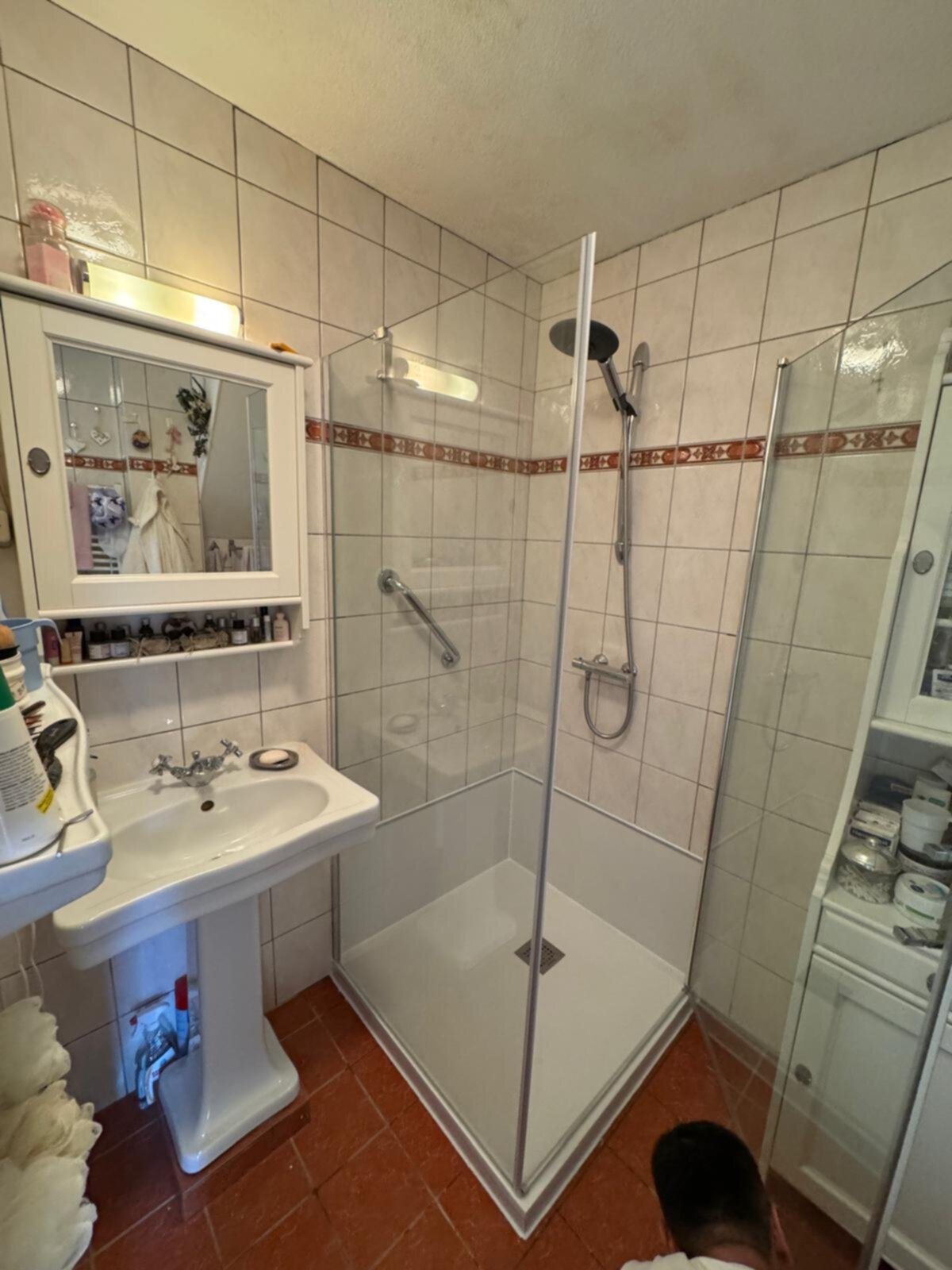 Badkamer met witte tegelwanden en rode vloertegels, douche, wastafel en spiegel