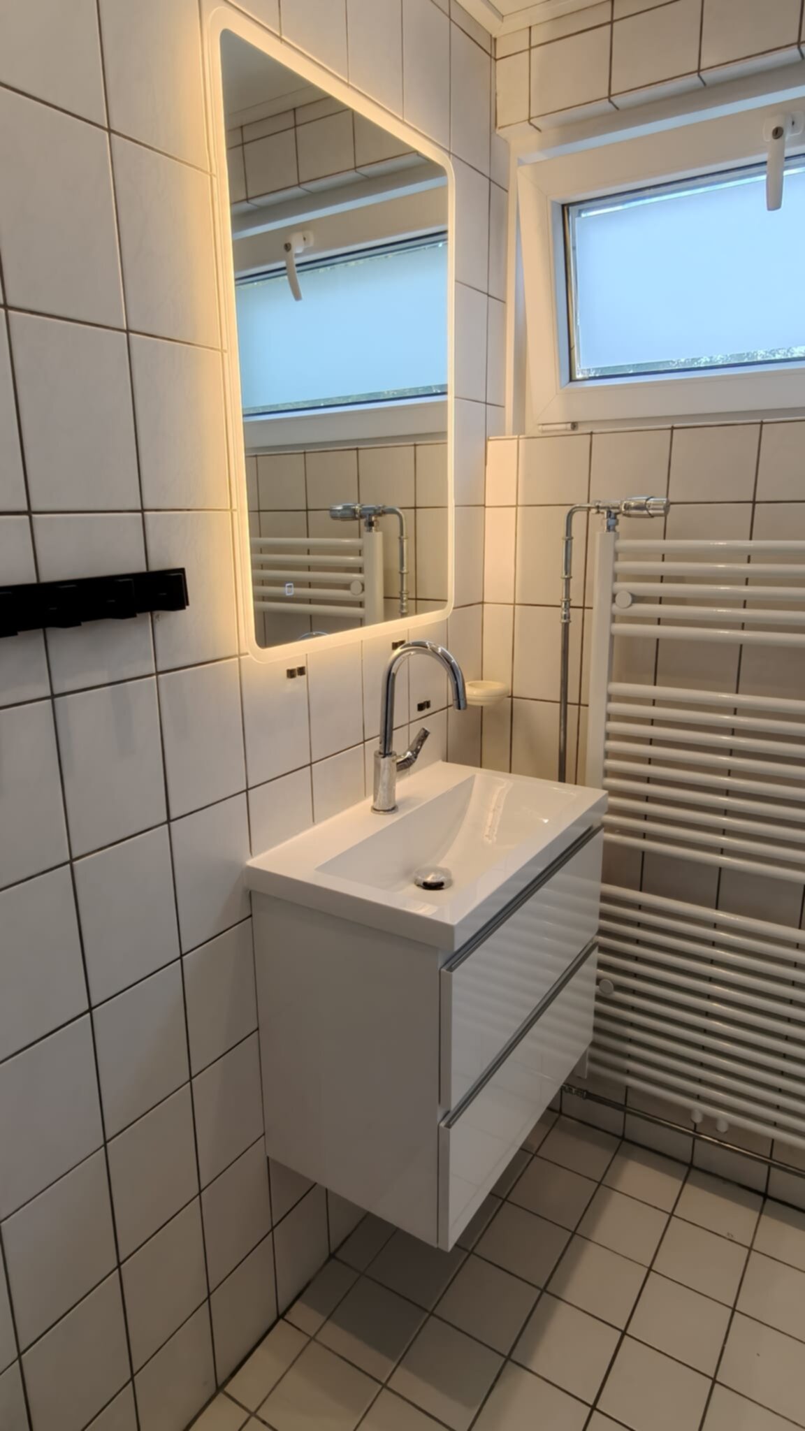 Wit betegelde badkamer met wastafel, spiegel en verwarming