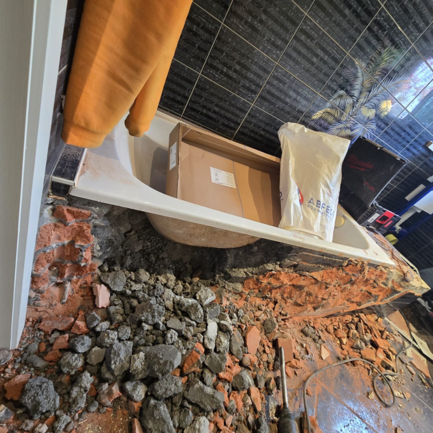 Sloop badkamer met stortbad, kartonnen doos en bouwmaterialen op de grond