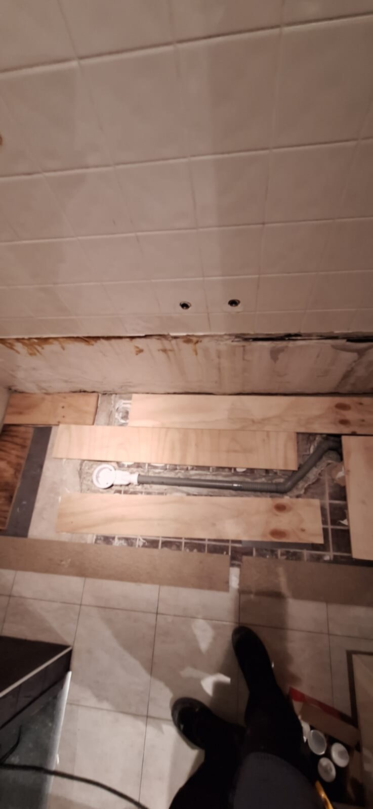 Badkamer renovatie, houten planken op de vloer, grijze en bruine tegels, pijpen zichtbaar