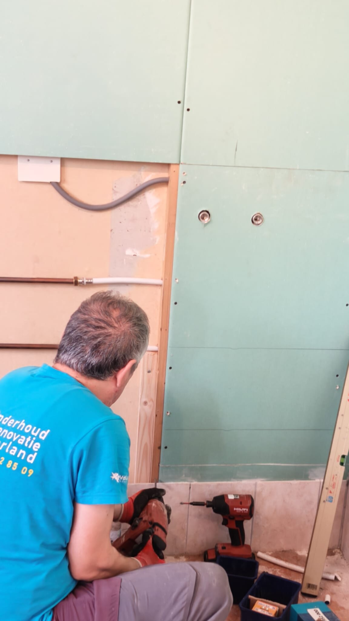 Man in blauwe trui werkt aan badkamer renovatie met gereedschap en materialen