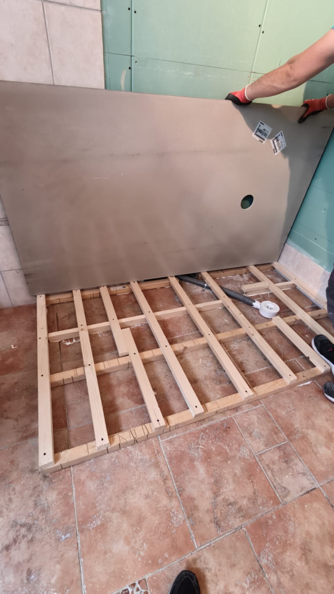 Een persoon plaatst een grote plaat tegen een muur in een badkamer tijdens renovatie