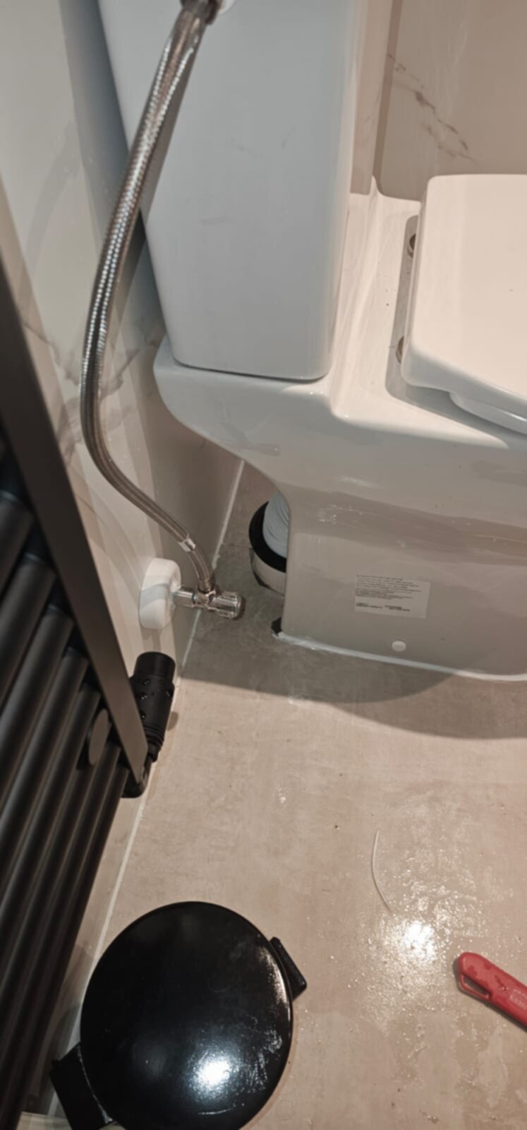 Wit toilet met metalen slang en zwarte pomp op grijze tegelvloer