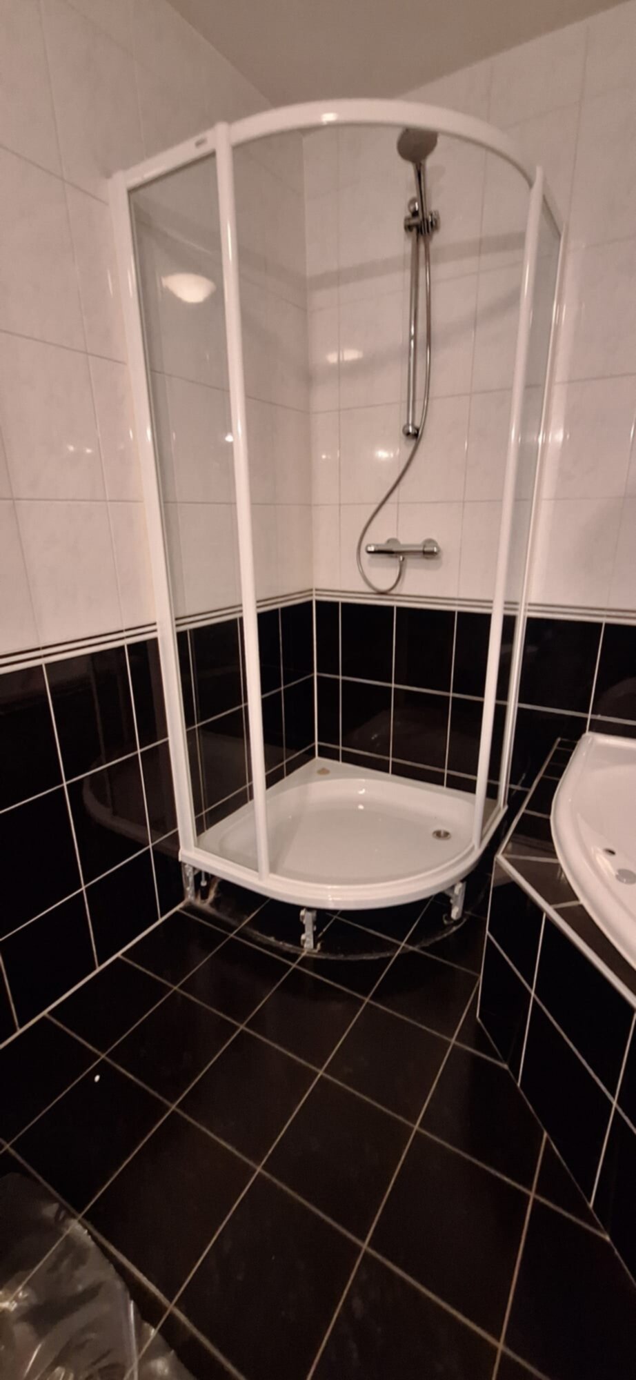 Douchecabine met witte frame en glazen wanden in een badkamer met zwart-wit betegeling