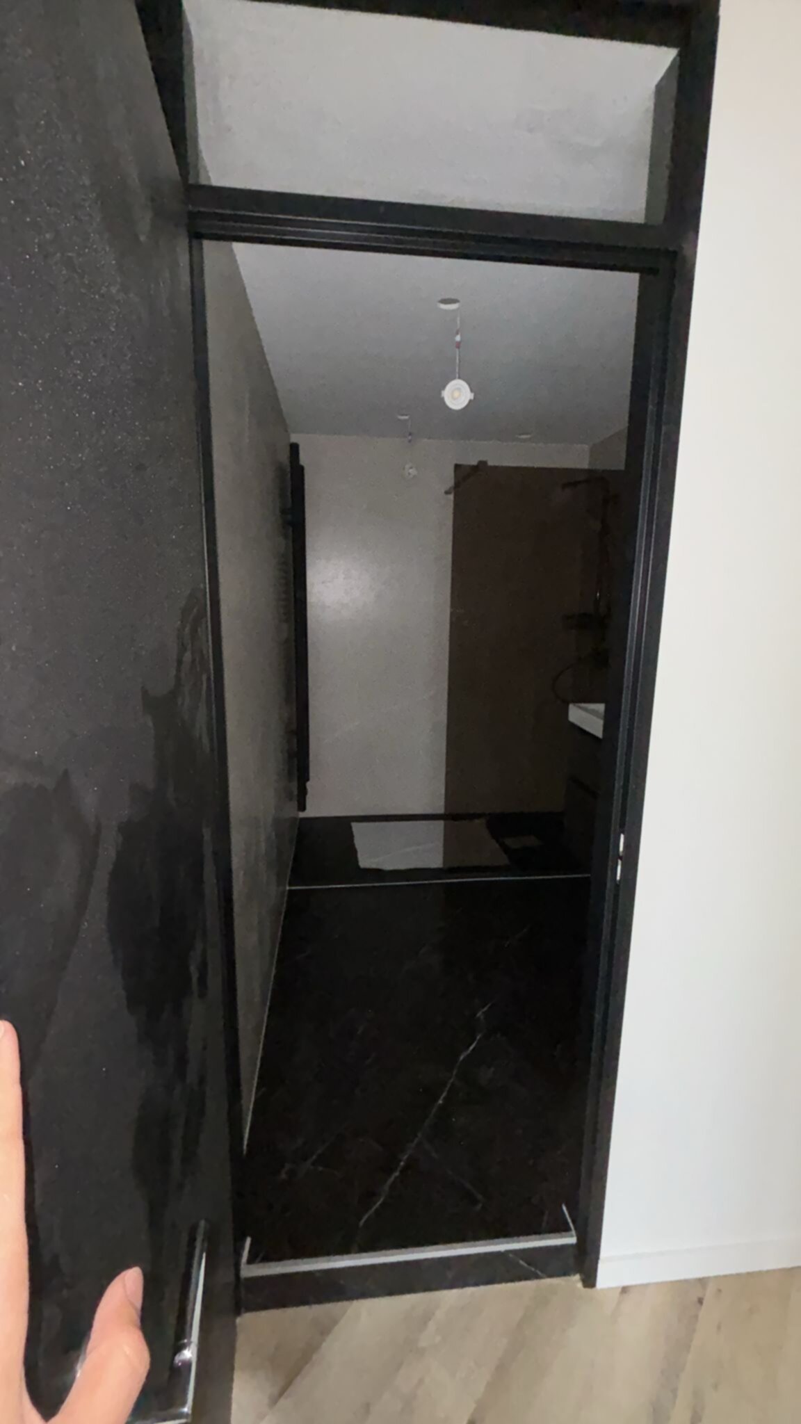 Douchecabine met zwarte glazen wand en deur, witte muren en houten vloer