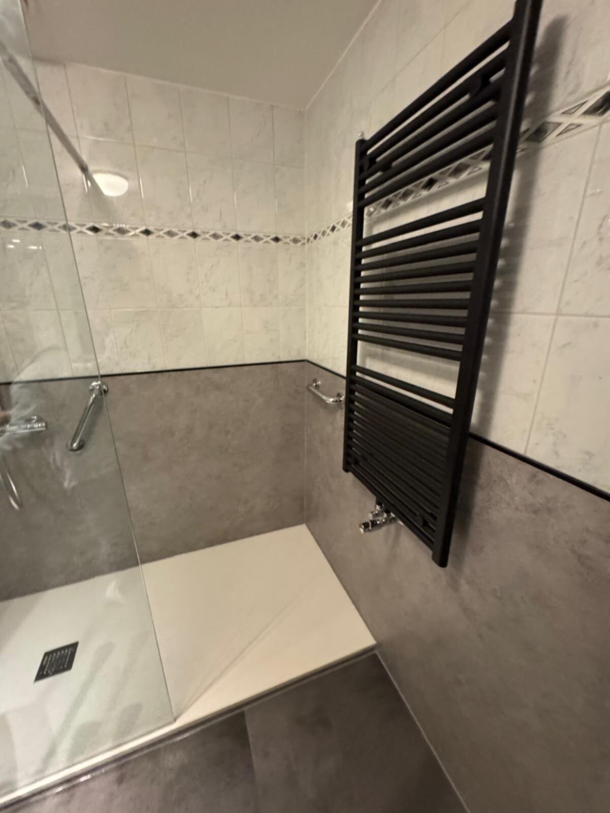 Douchehoek met zwarte verwarmingsradiator en glazen deur in moderne badkamer
