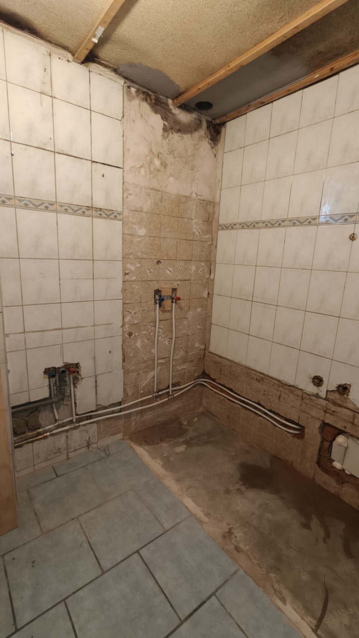 Slechte staat badkamer met beschadigde tegels en zichtbare leidingen