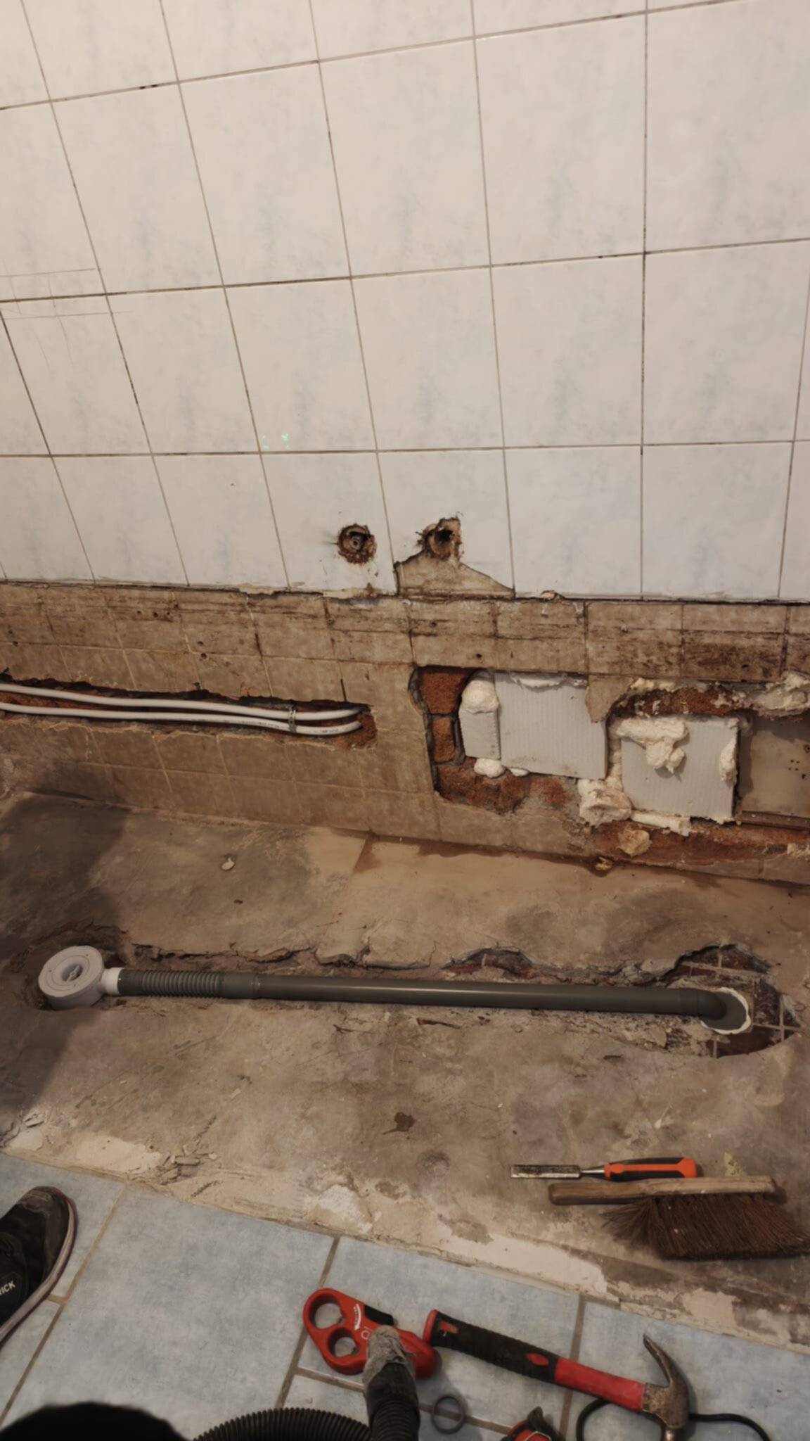 Sleuf in badkamerwand met blootgelegde leidingen en gereedschap