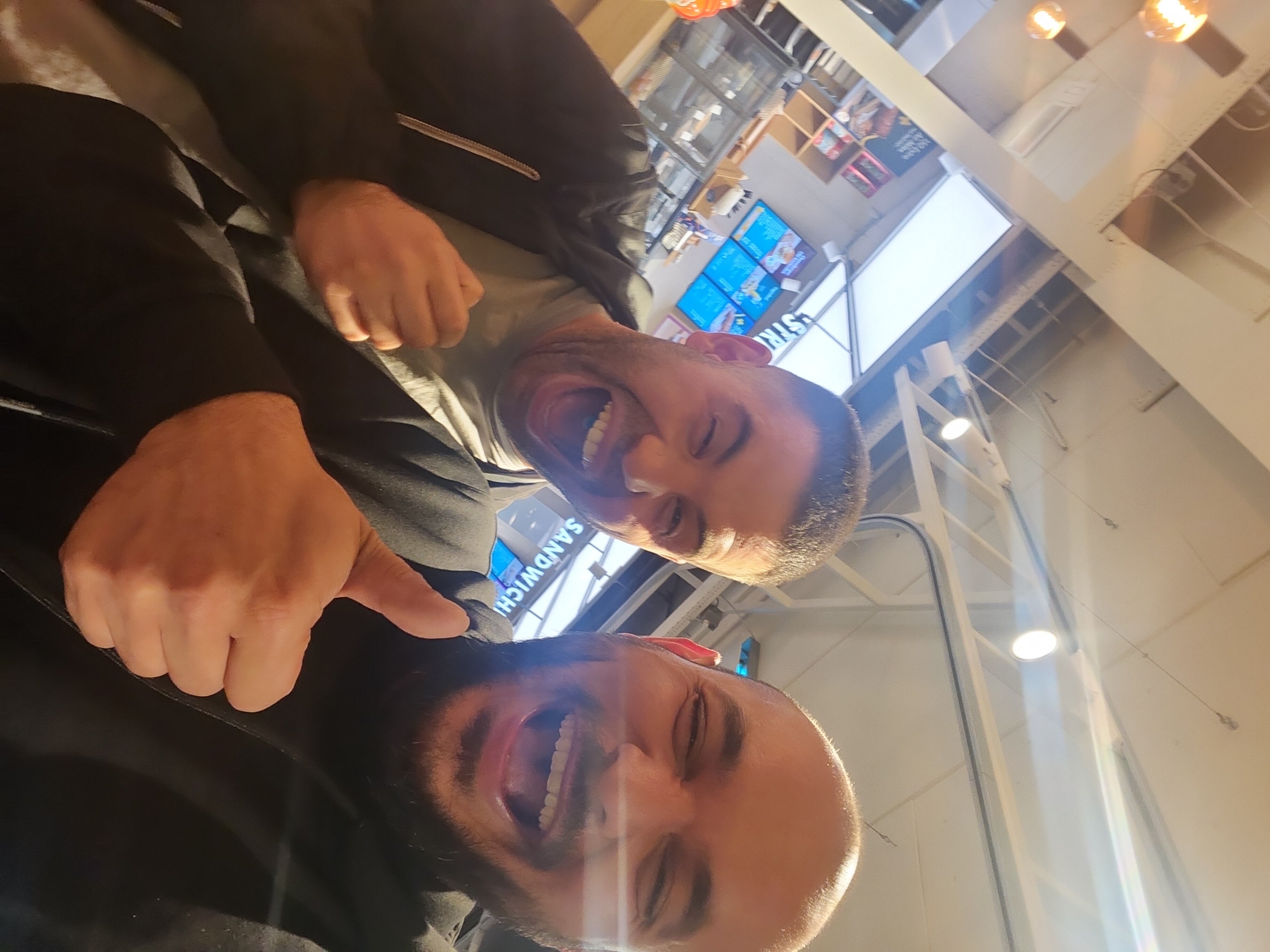 Twee mannen lachen en geven duim omhoog in een foodcourt