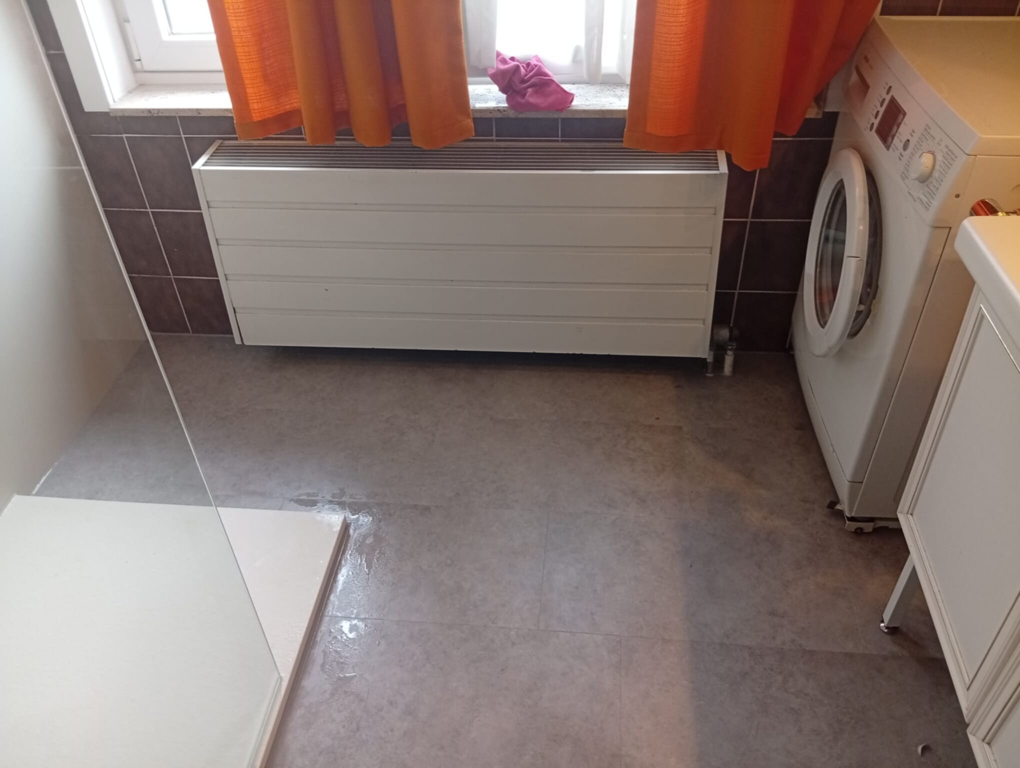 Grijze tegelvloer en bruine wandtegels in kleine badkamer met wasmachine en radiator