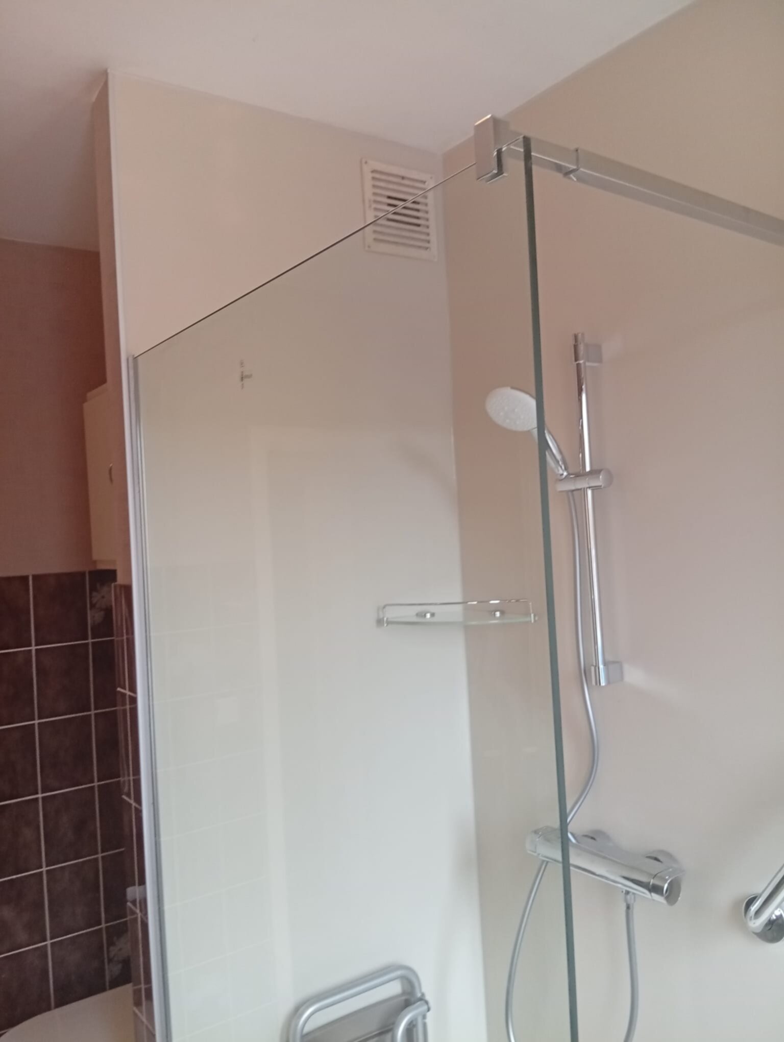 Douche met glazen schuifdeur en chroomkranen in beige en bruine tegelwand
