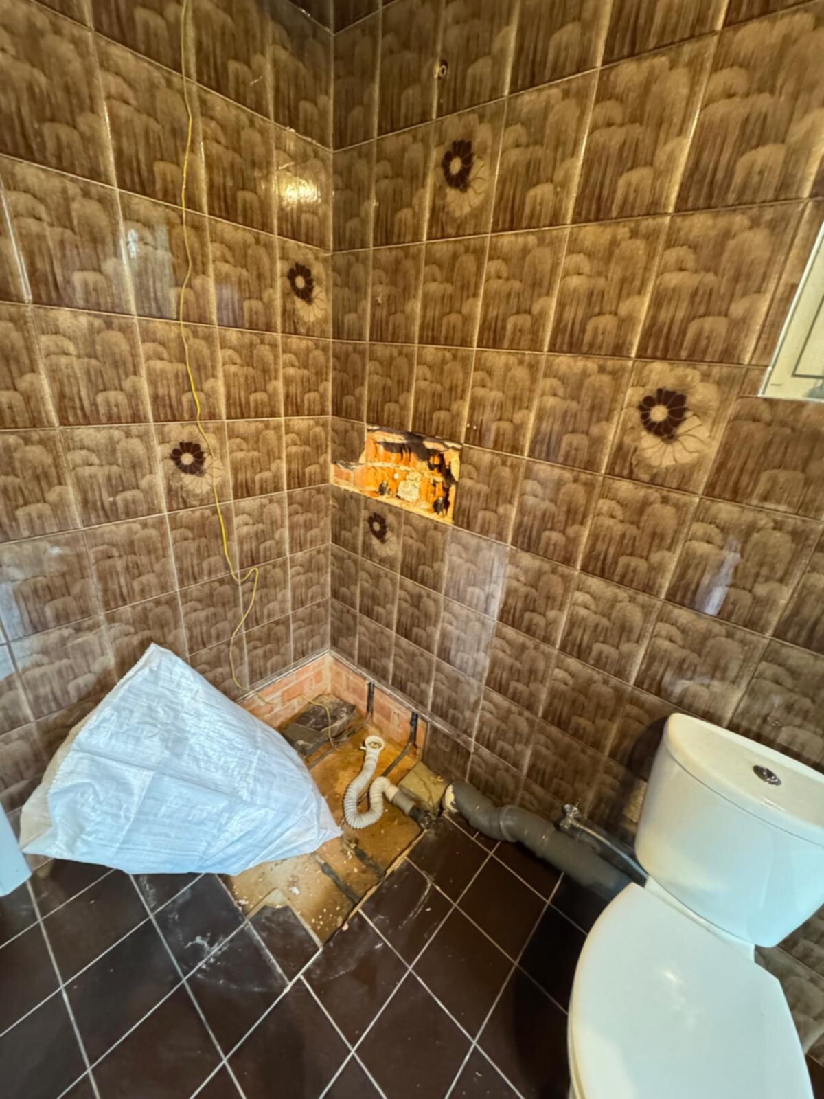 Slechte staat badkamer met bruine tegels en kapotte douche
