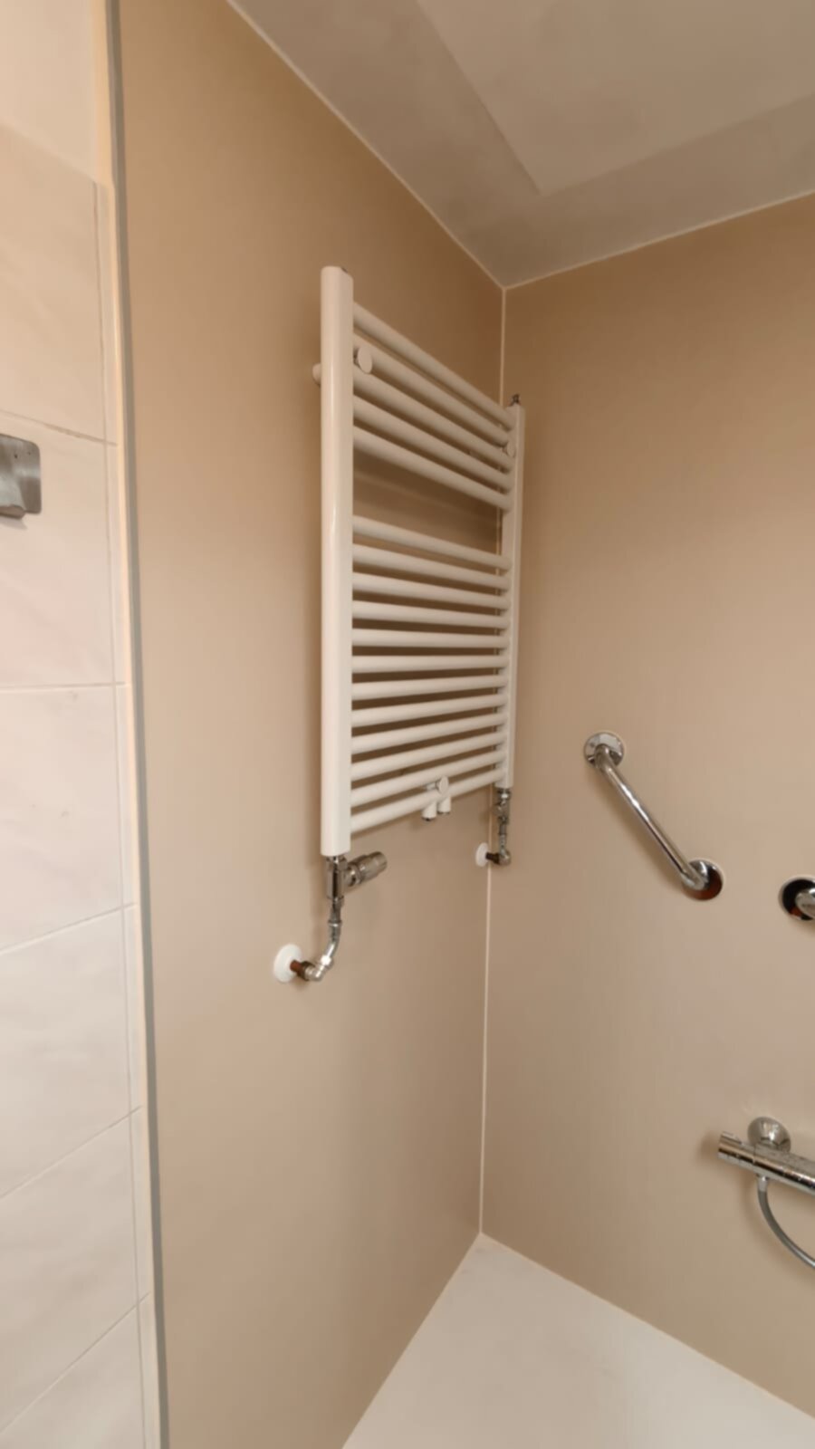 Witte verwarmingsradiator in beige badkamer met betegelde wand en metalen grepen