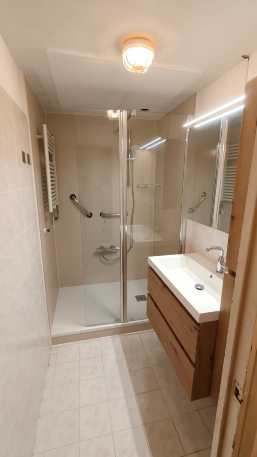 Badkamer met beige tegels, douche, wastafel en spiegel