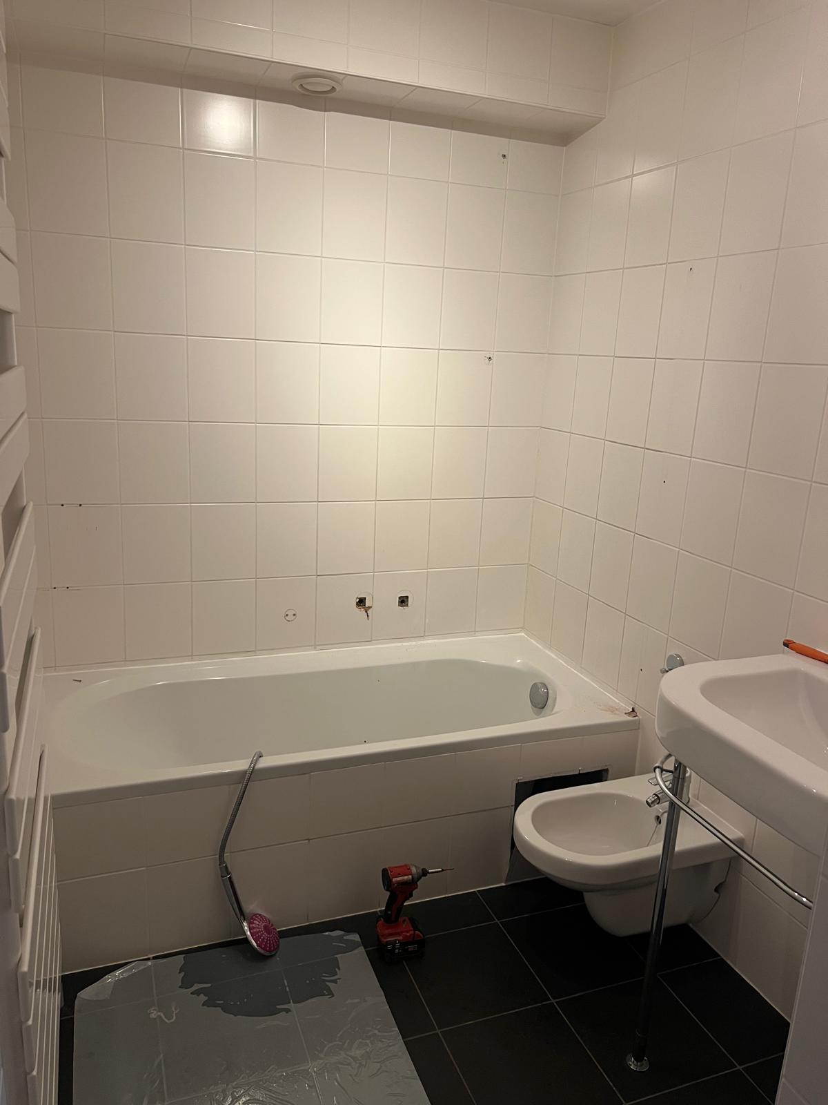 Gedateerde badkamer met wit sanitair en witte tegels, klaar voor renovatie.